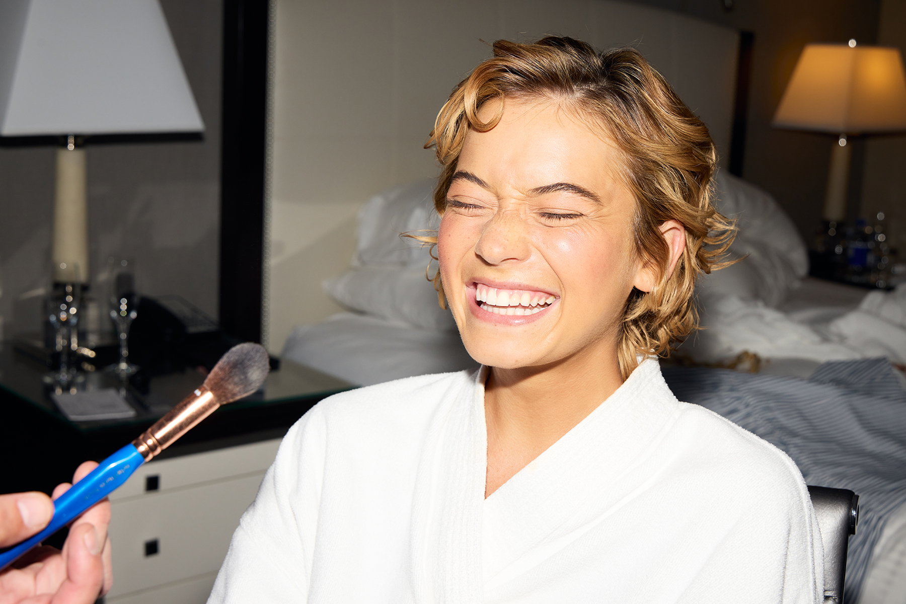 Image from Sophie Telegadis&#039; TIFF photo diary. She is sitting in the glam chair wearing a white robe and laughing as she gets final makeup touches.