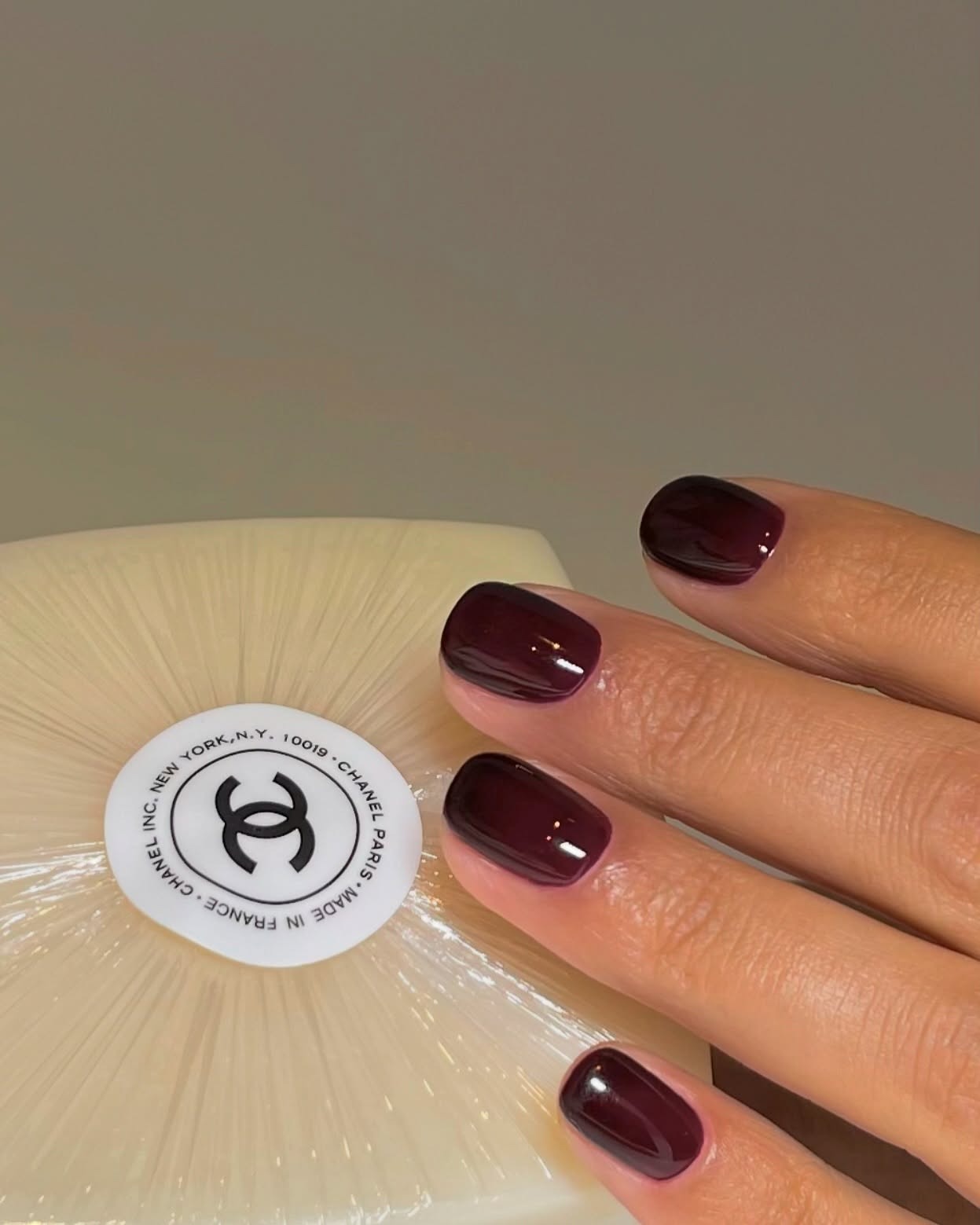 A close up of a hand with short dark red nails holding a Chanel soap