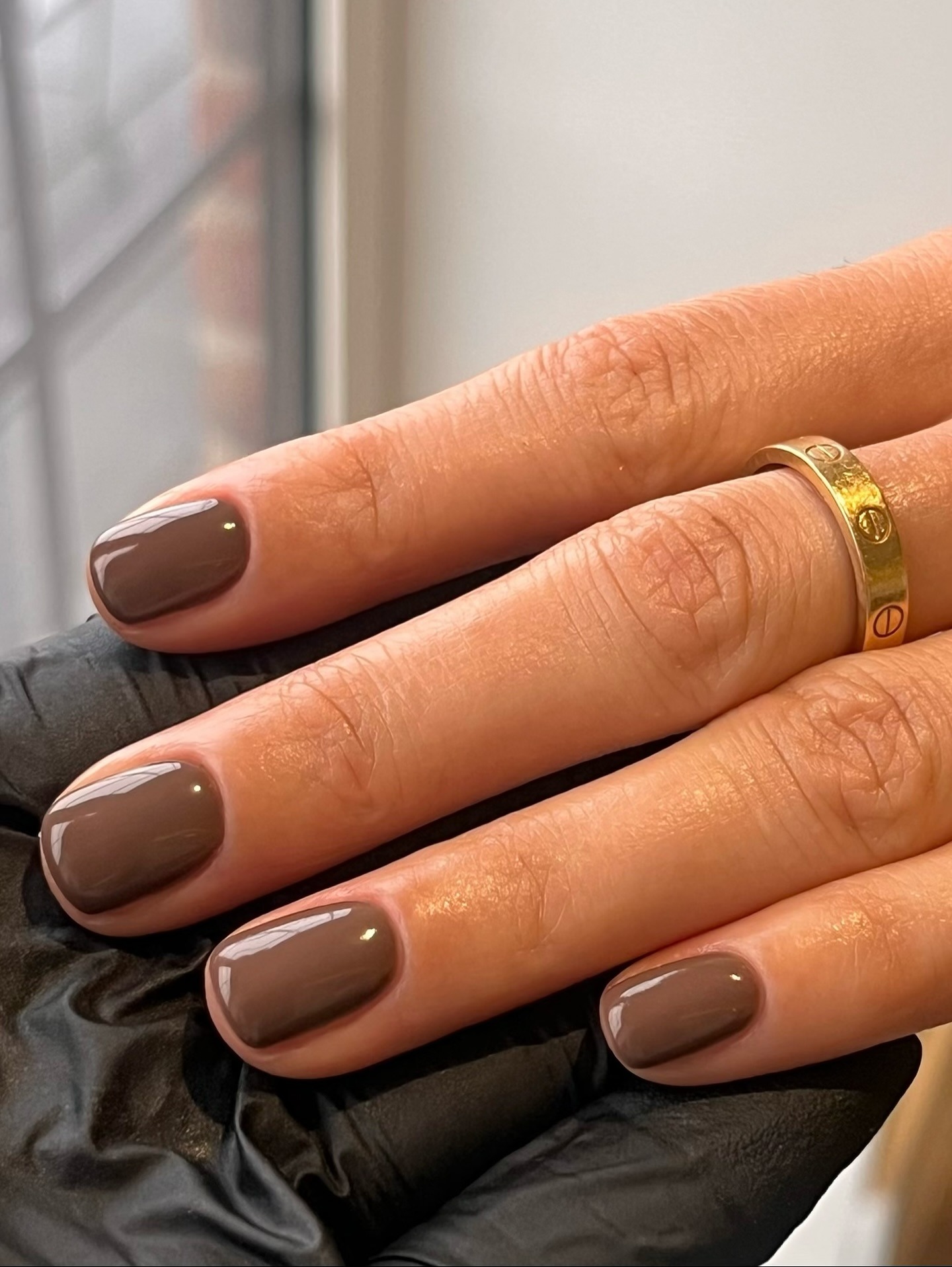 A close up of short dark brown nails and a gold Cartier ring on a finger