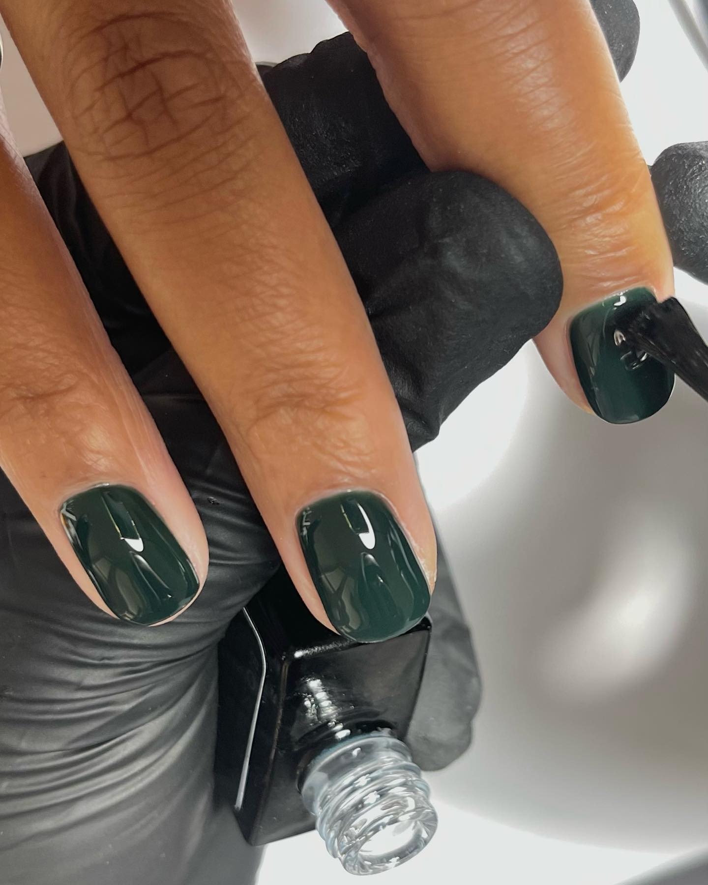 A close up photo of a nail tech painting short nails with dark green polish