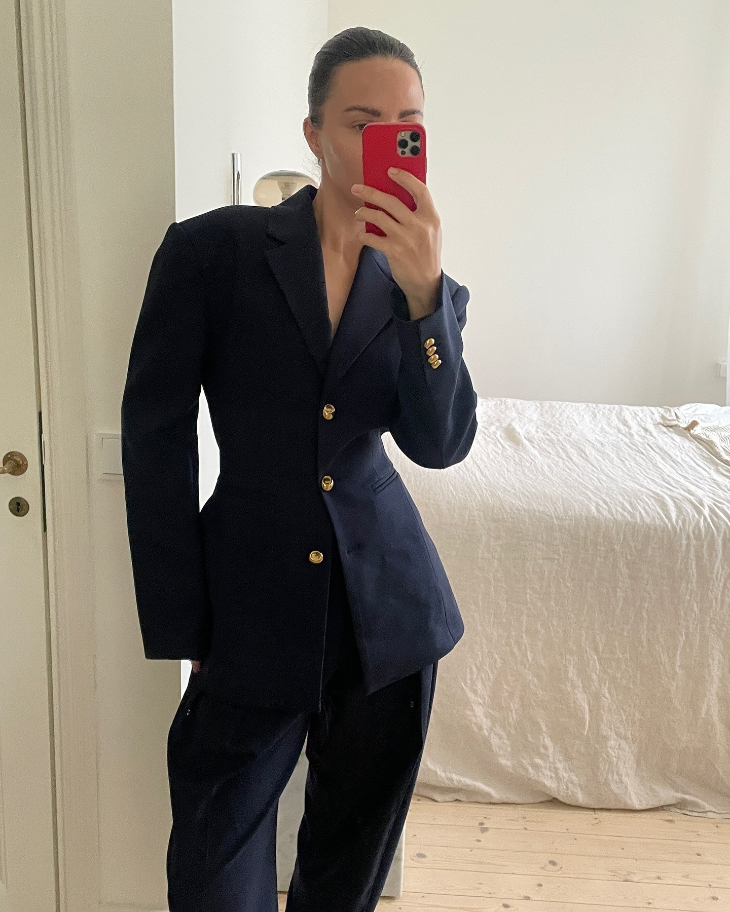 style influencer Johanna Piispa poses for a mirror selfie wearing a waisted navy blazer suit jacket with yellow-gold buttons and matching navy pants