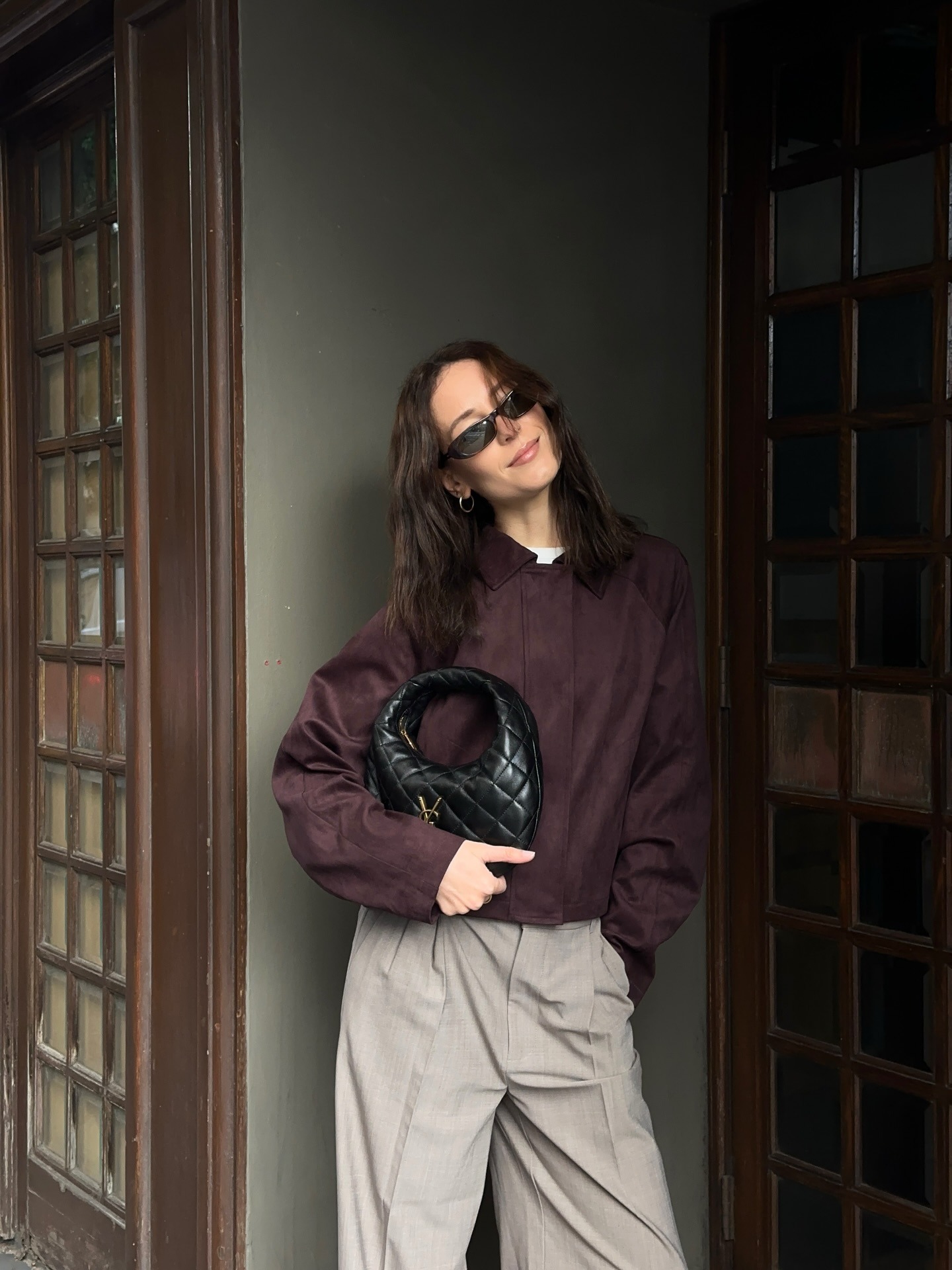 Woman wears burgundy jacket, beige trousers and carries Saint Laurent black quilted bag