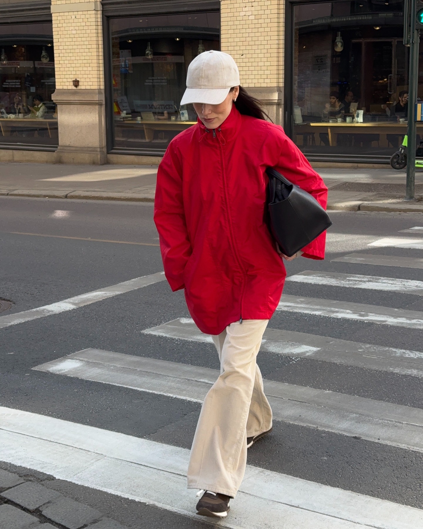 Influencer @annabelrosendahl crosses the street wearing a red jacket with cream trousers and brown trainers.