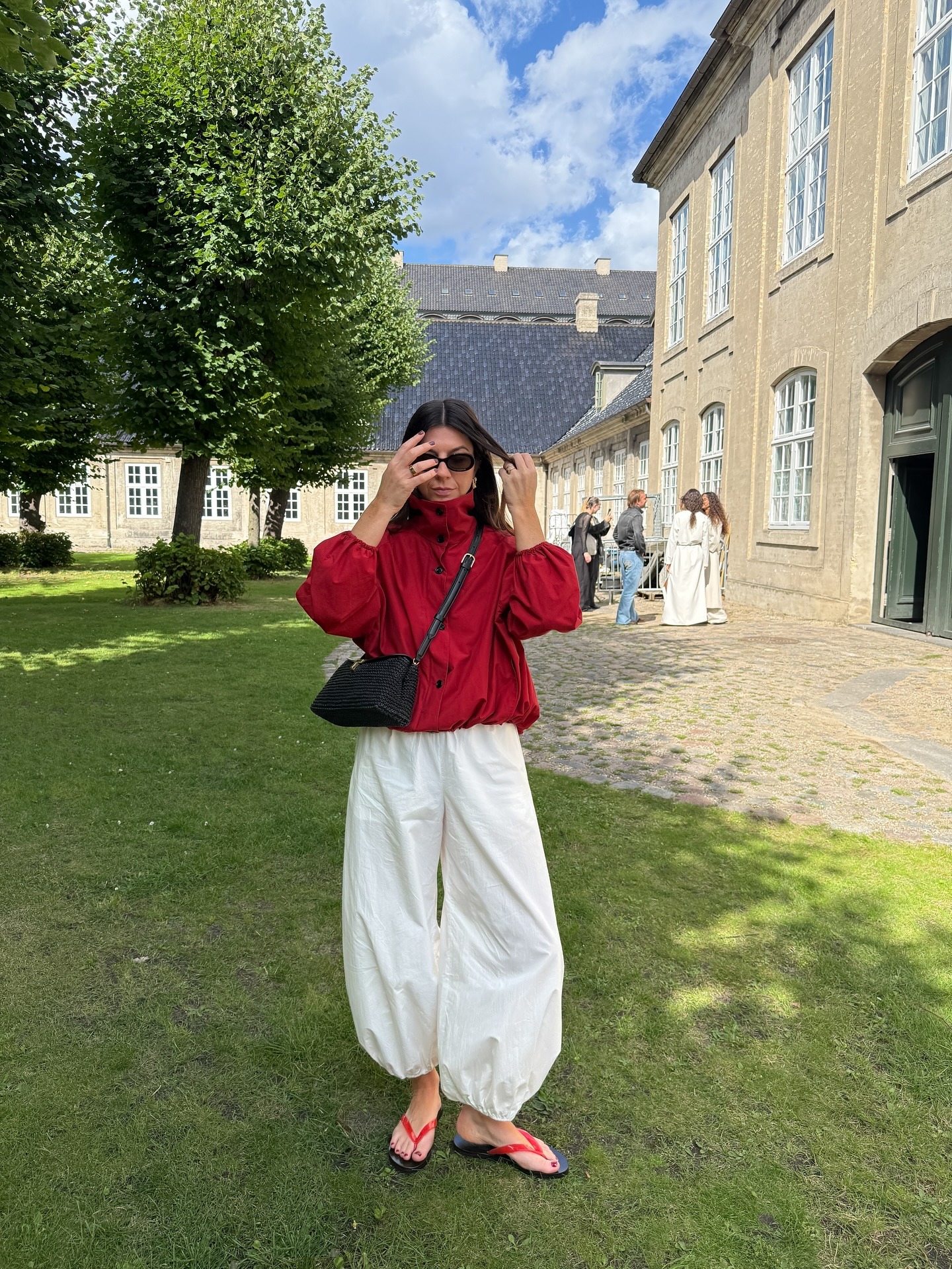 Influencer @francescasaffari stands outside wearing a red jacket with white trousers and red flip-flops.