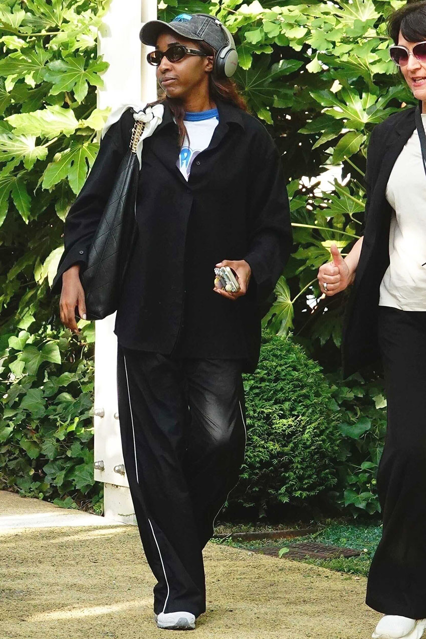 Ayo Edebiri wearing a gray baseball cap, white t-shirt, black button-down, black track pants, and white sneakers