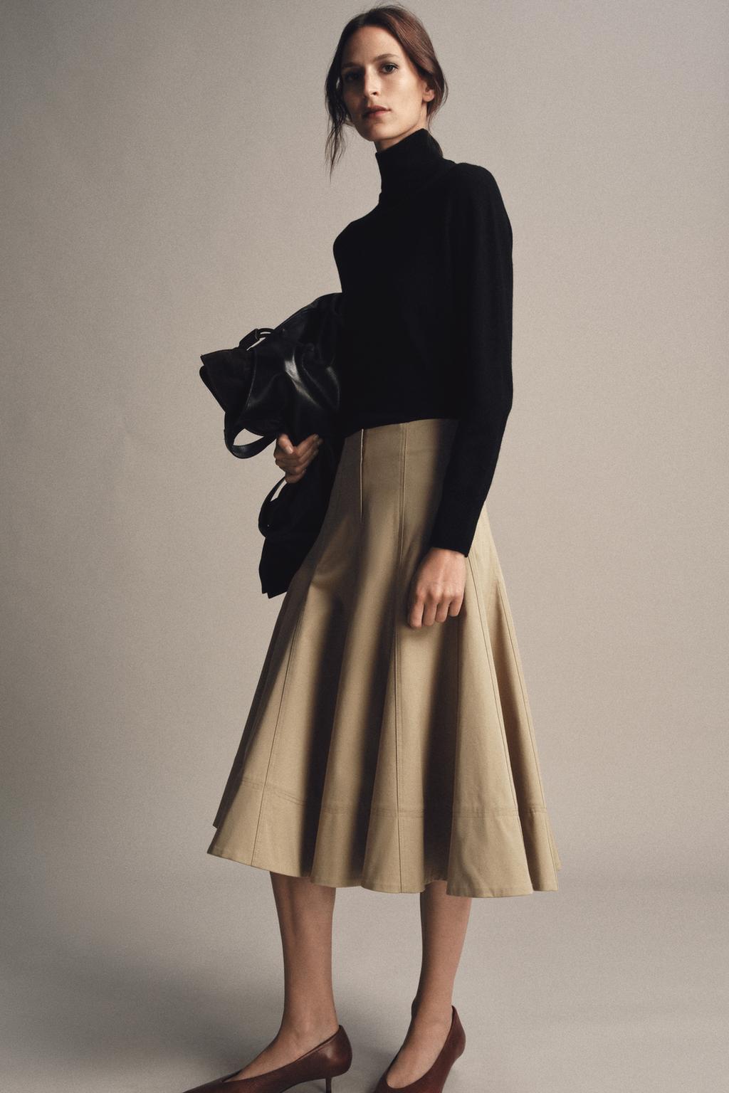 model wears black turtleneck sweater, zara midi trench skirt, and kitten heels while posing with a black oversized leather tote