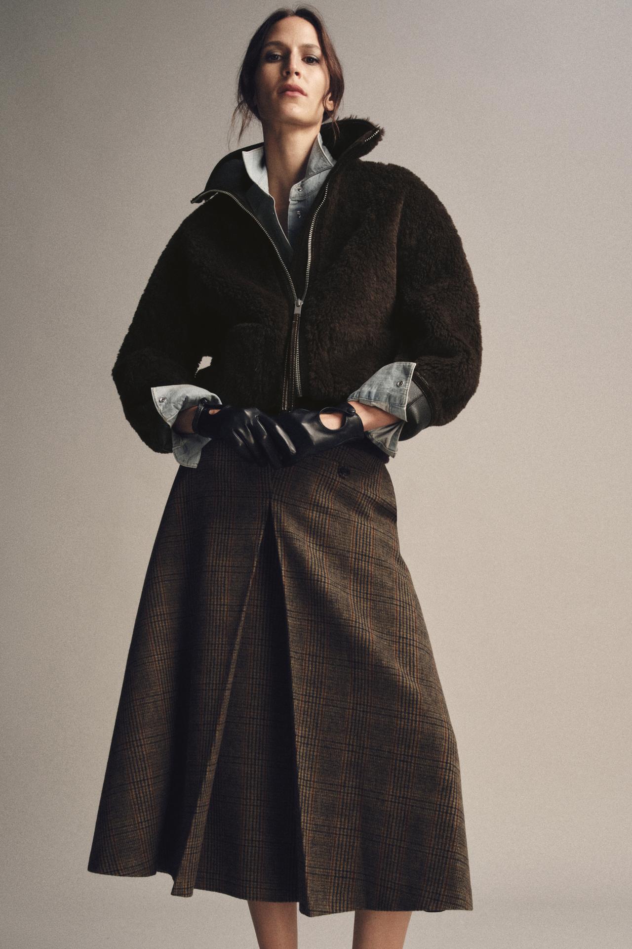 model wears skirt, faux fur jacket, denim shirt and leather gloves while posing