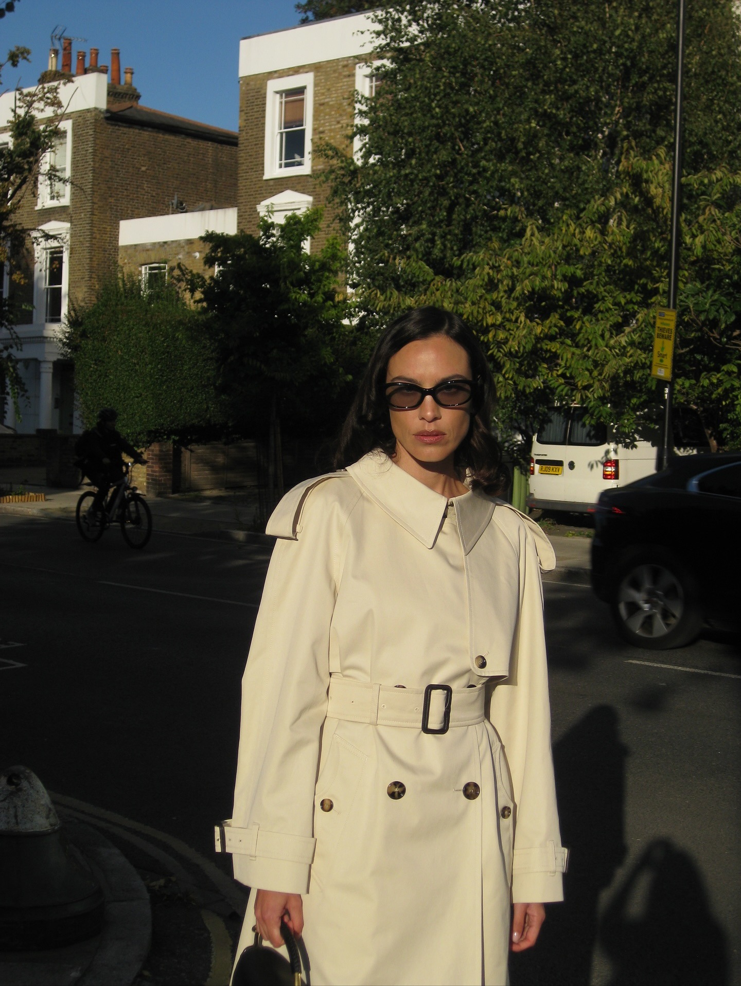 Alexa Chung wears a cream trench coat with sunglasses.