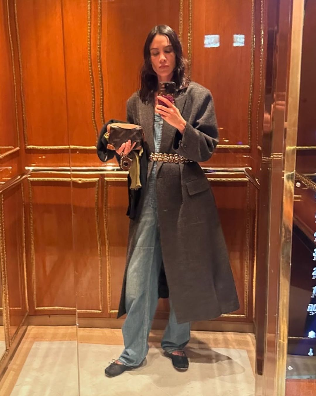 Alexa Chung wears grey coat cinched in with a belt and black flats.