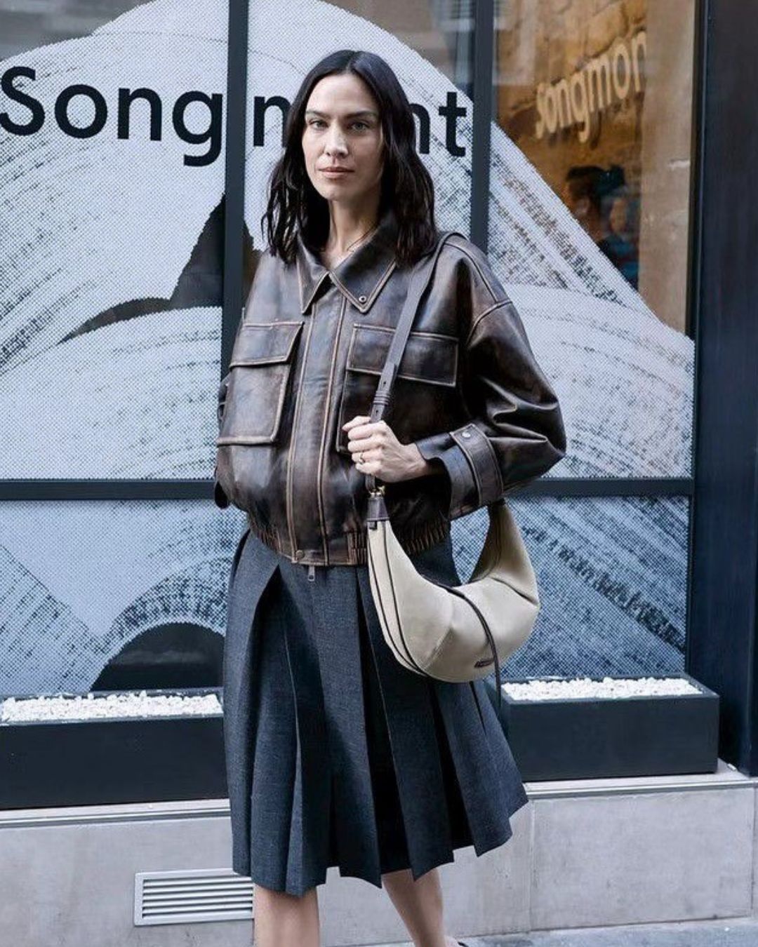 Alexa Chung wears a brown leather jacket with a grey pleated skirt.