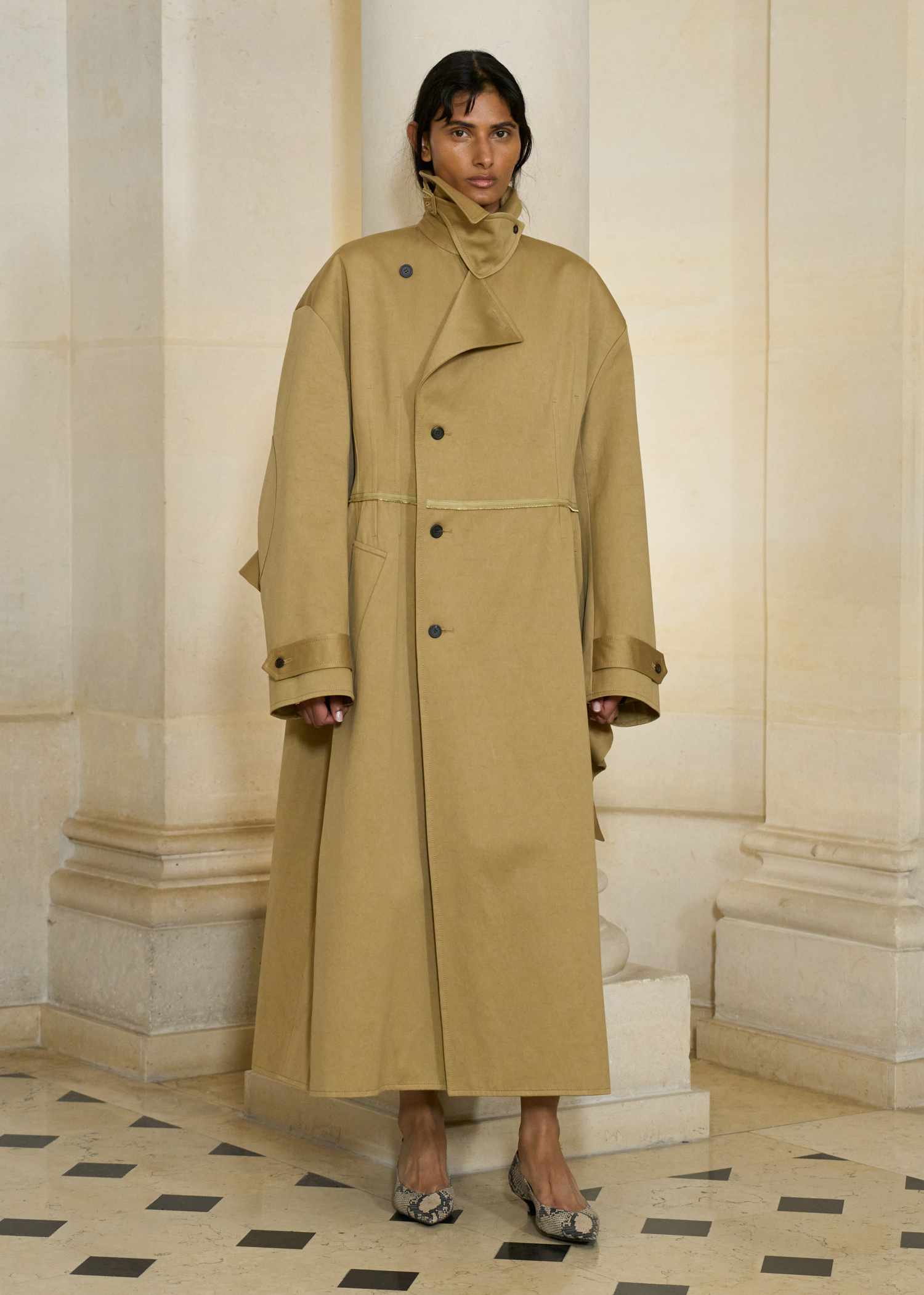 A model at the S/S 26 Carven show wearing a maxi-length trench coat with snakeskin pumps.