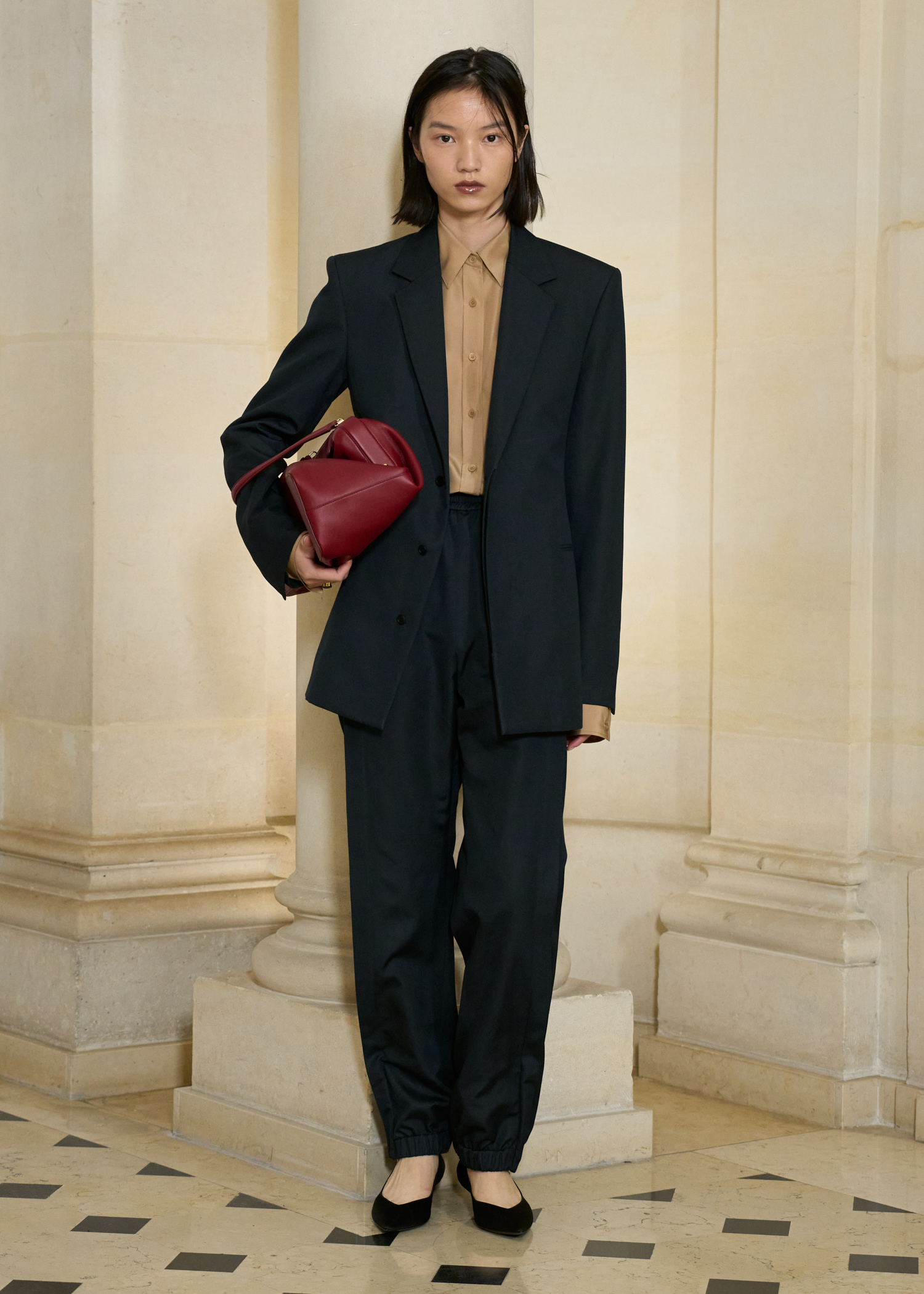 A model at the S/S 26 Carven show wearing a black suit with a burgundy bag and black pumps.