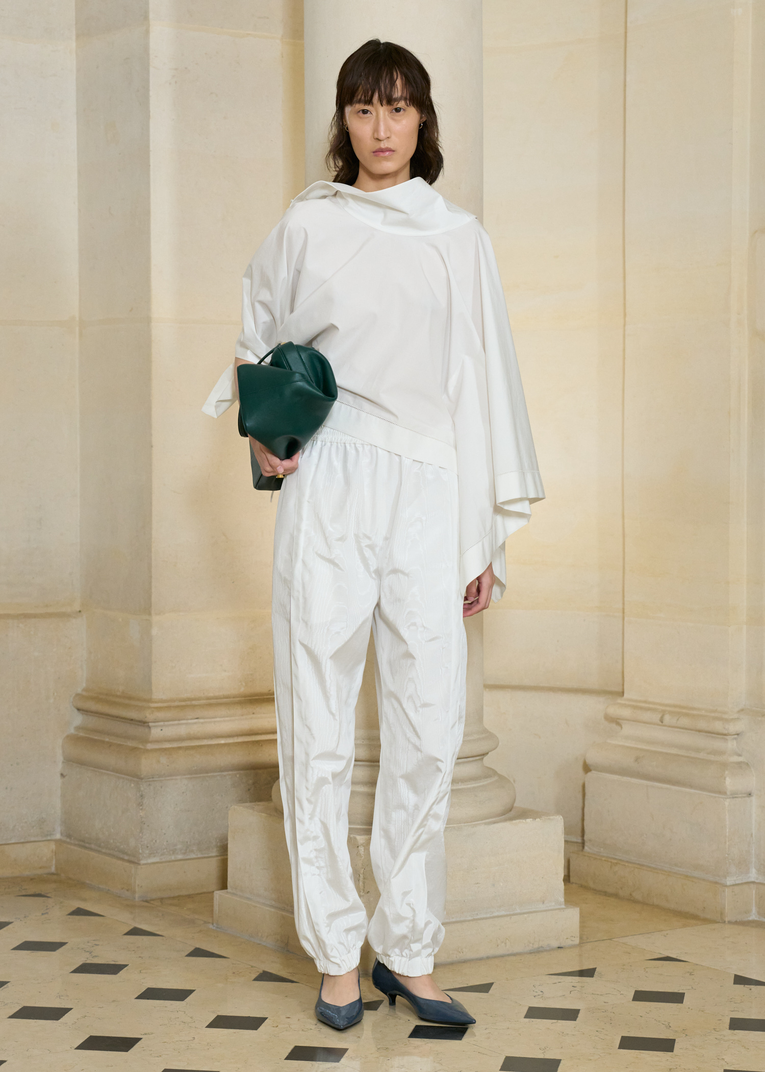 A model at the SS26 Carven show wearing a white poplin set with a green bag and pumps.