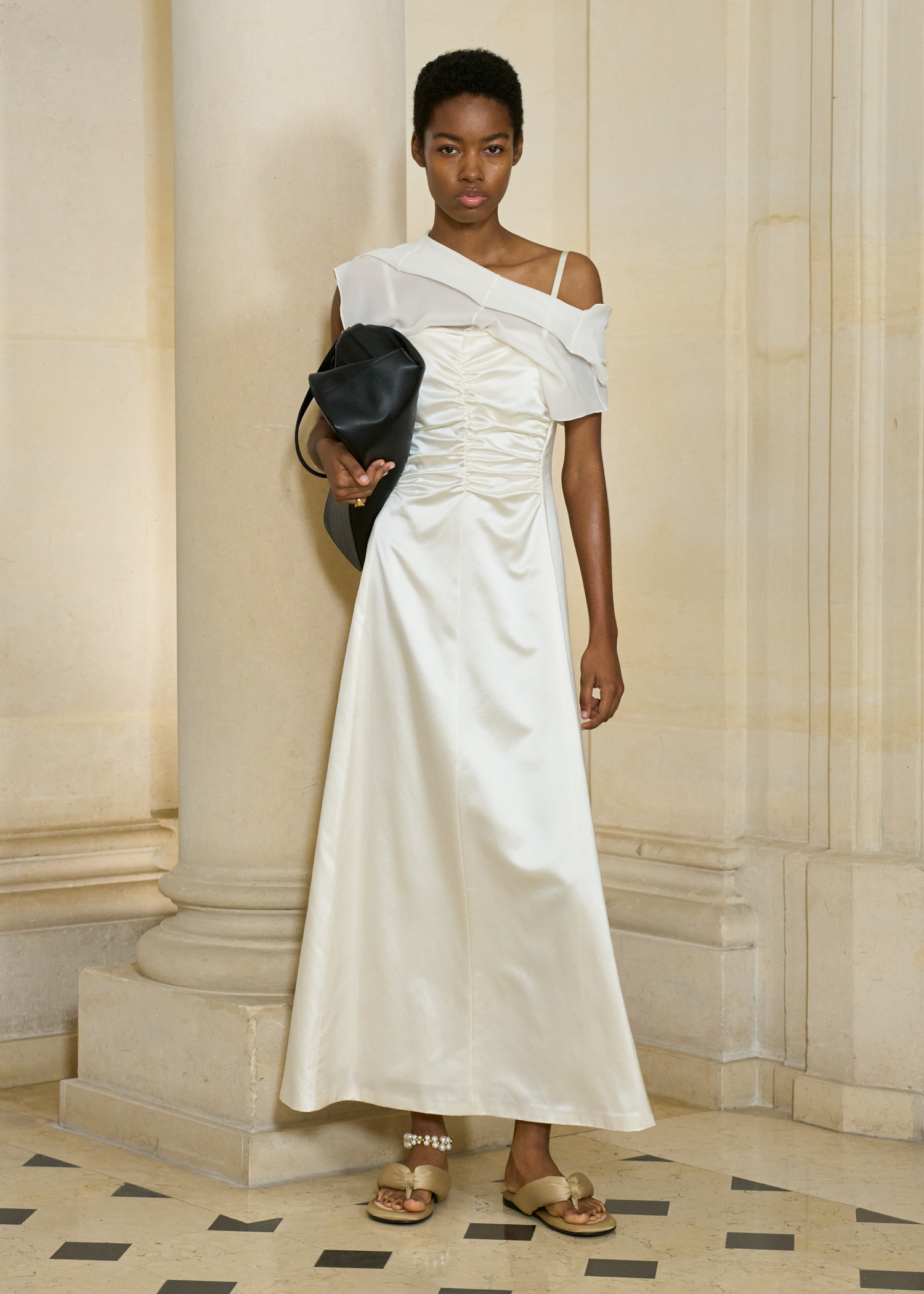A model in the S/S 26 Carven show wearing a cream satin dress with gold, satin, padded flip-flops.
