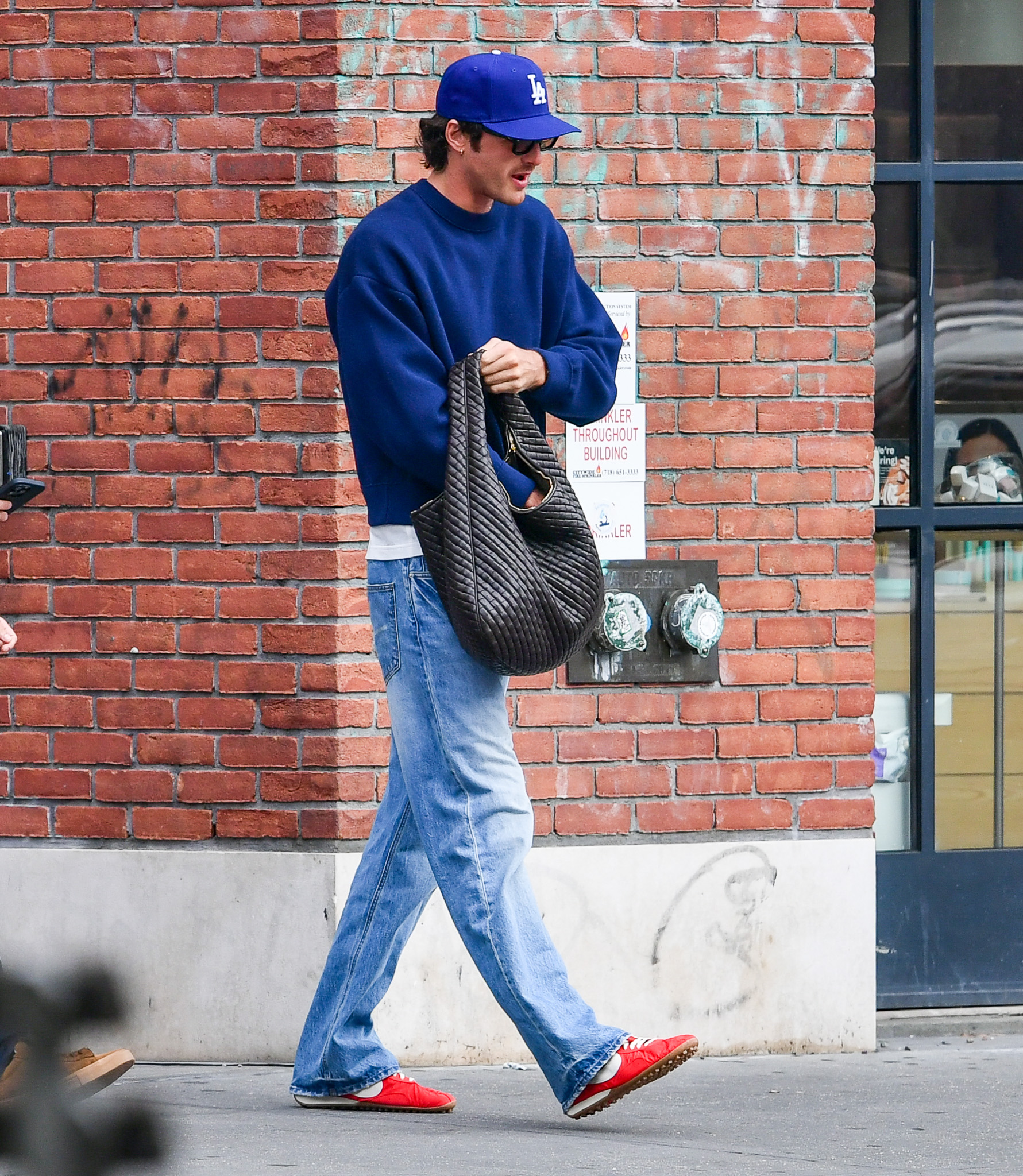 10/20/2025: Jacob Elordi is spotted carrying a large Bottega Veneta handbag in New York City. The American actor wore a blue cap, matching cropped sweatshirt, jeans, and red Nike trainers.