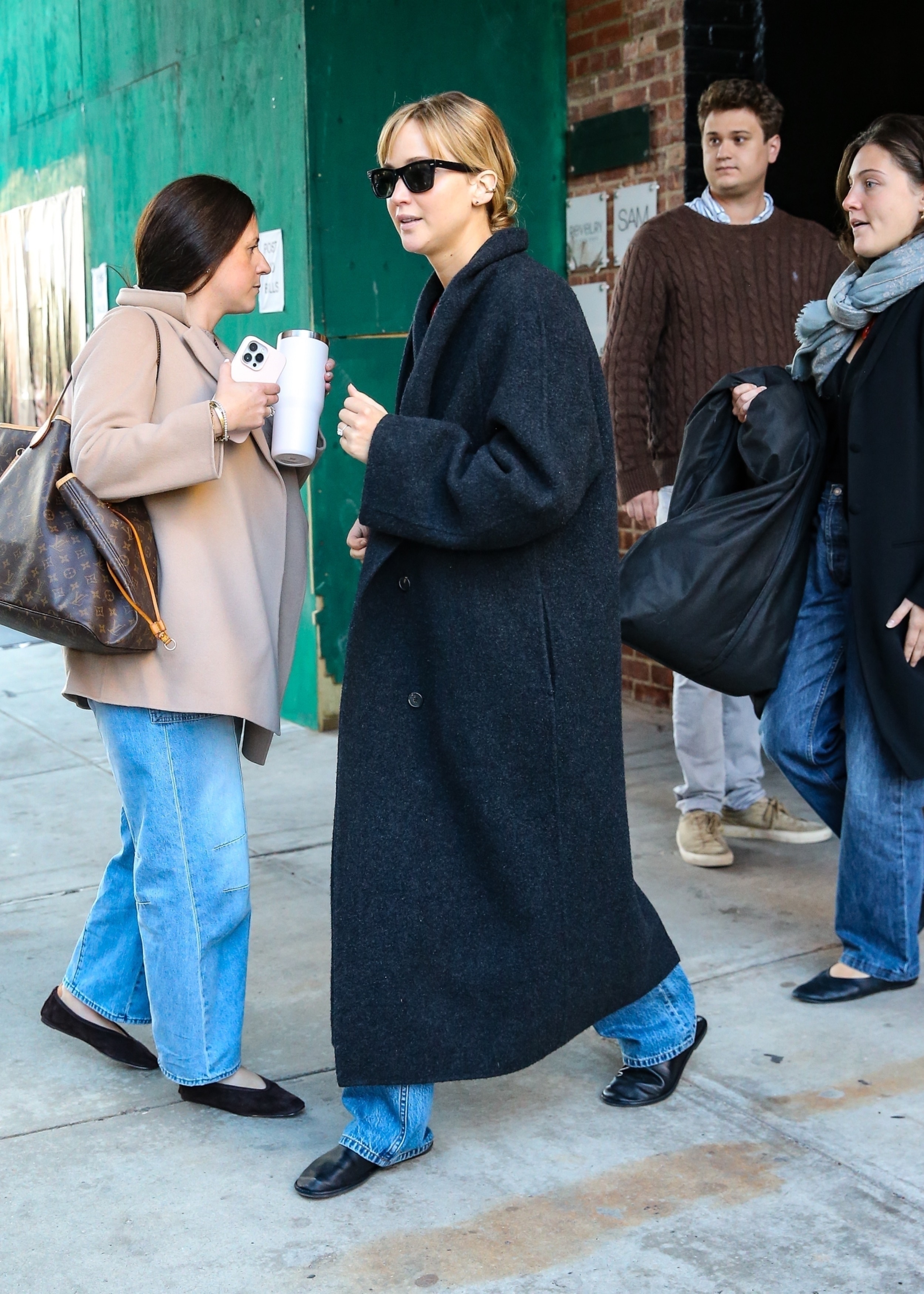 Jennifer Lawrence walks outside wearing a grey wool coat, blue jeans and rounded-toe flat shoes.