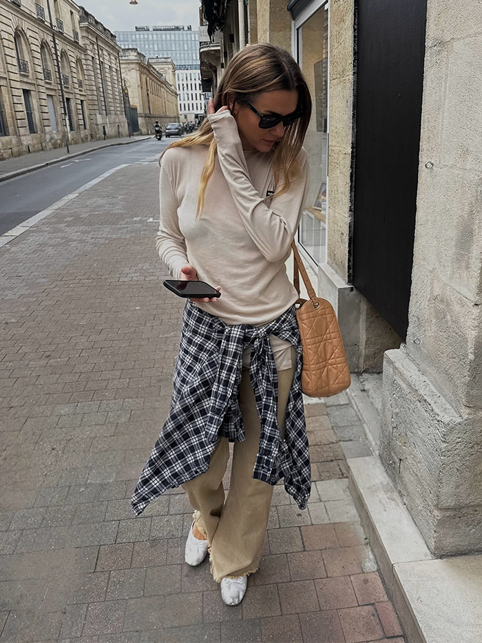 anne wears long sleeve t shirt, tan jeans, white ballet flats, and a plaid button-down shirt around the waist