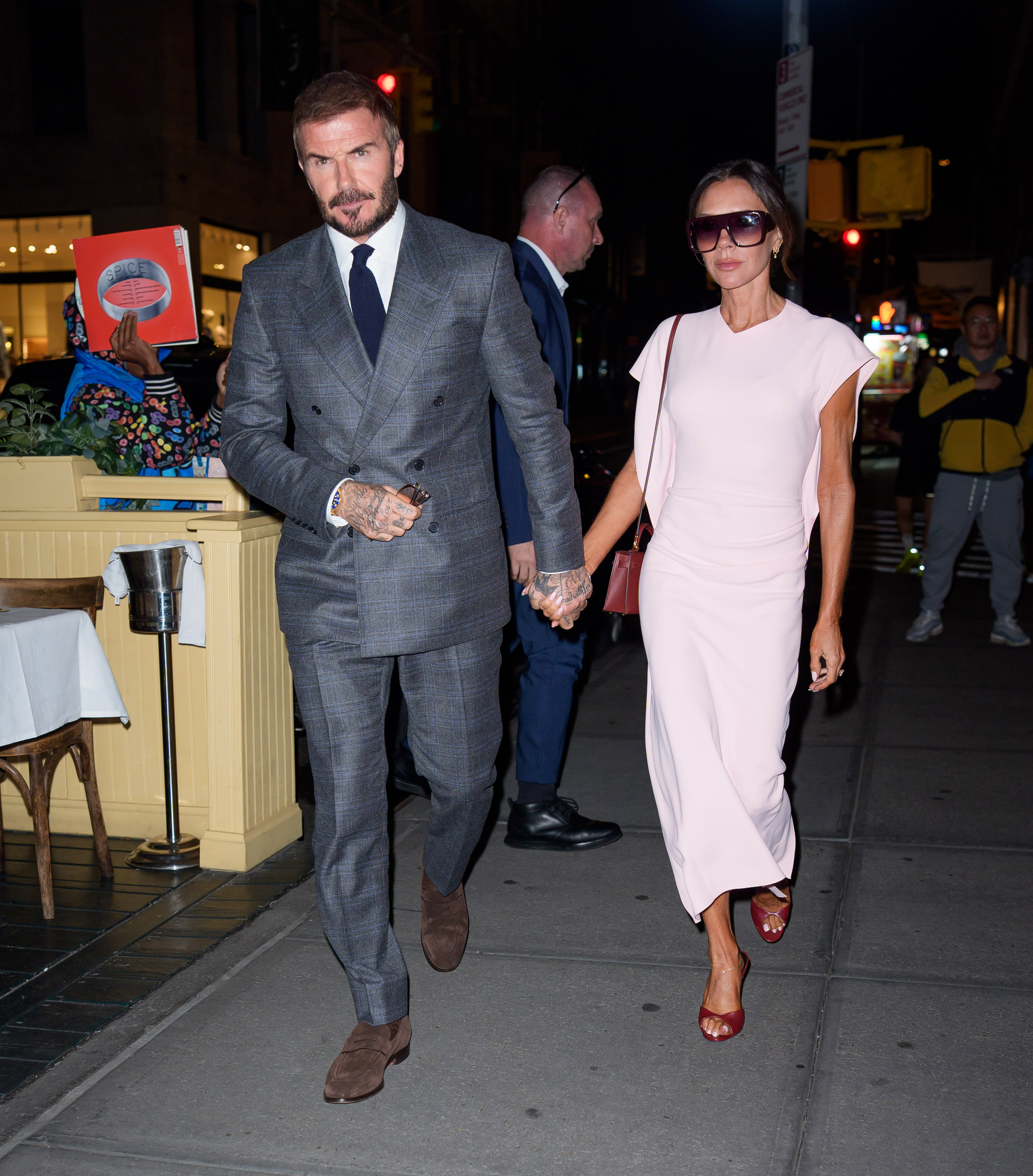 Victoria Beckham holds hands with David Beckham wearing a pink dress, burgundy heels and a burgundy bag.