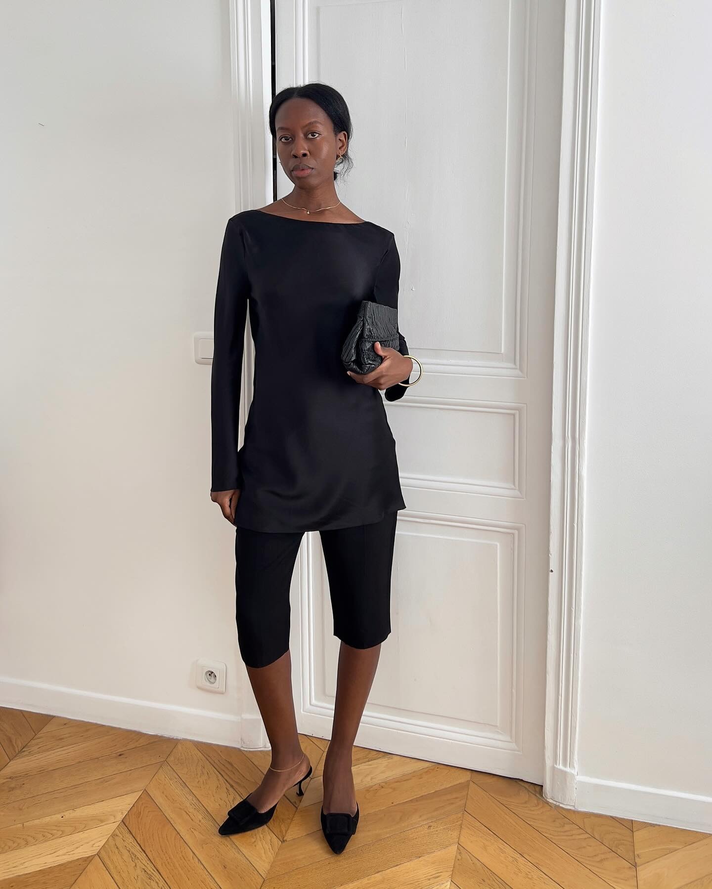 Influencer @sylviemus_ wears a black satin blouse with black capri pants and heeled mules.