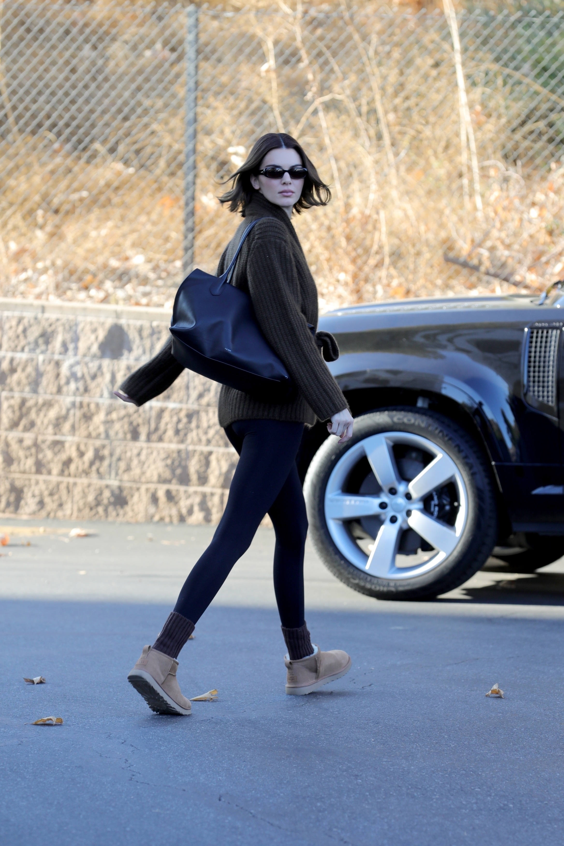 Kendall Jenner wears black leggings, a brown sweater, and Uggs.