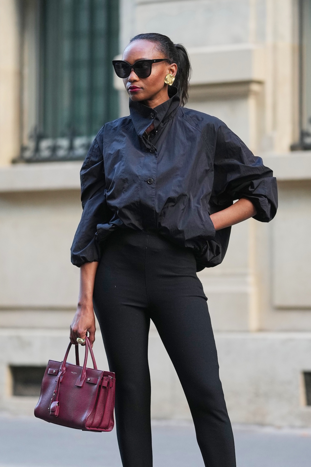 Street style image of a woman black sunglasses, a nylon cropped jacket, black leggings, and a red Saint Laurent bag