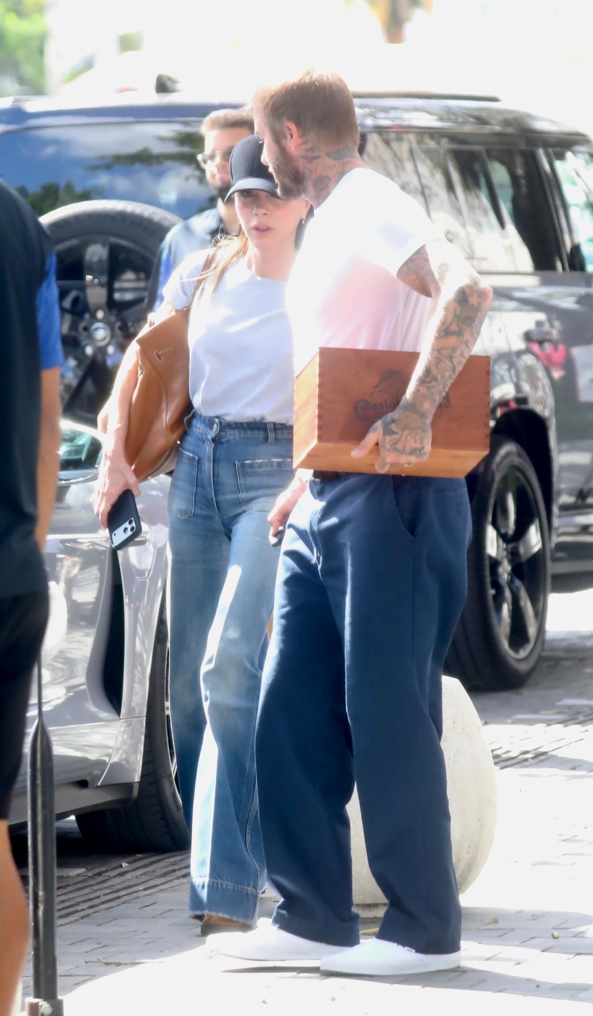 Victoria Beckham walks down the street with David Beckham, wearing high-waisted flared jeans with a white t-shirt.
