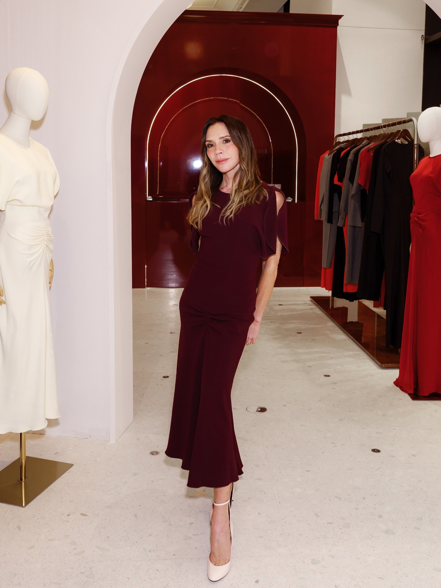 Victoria Beckham wears a burgundy dress with cream ankle strap heels.