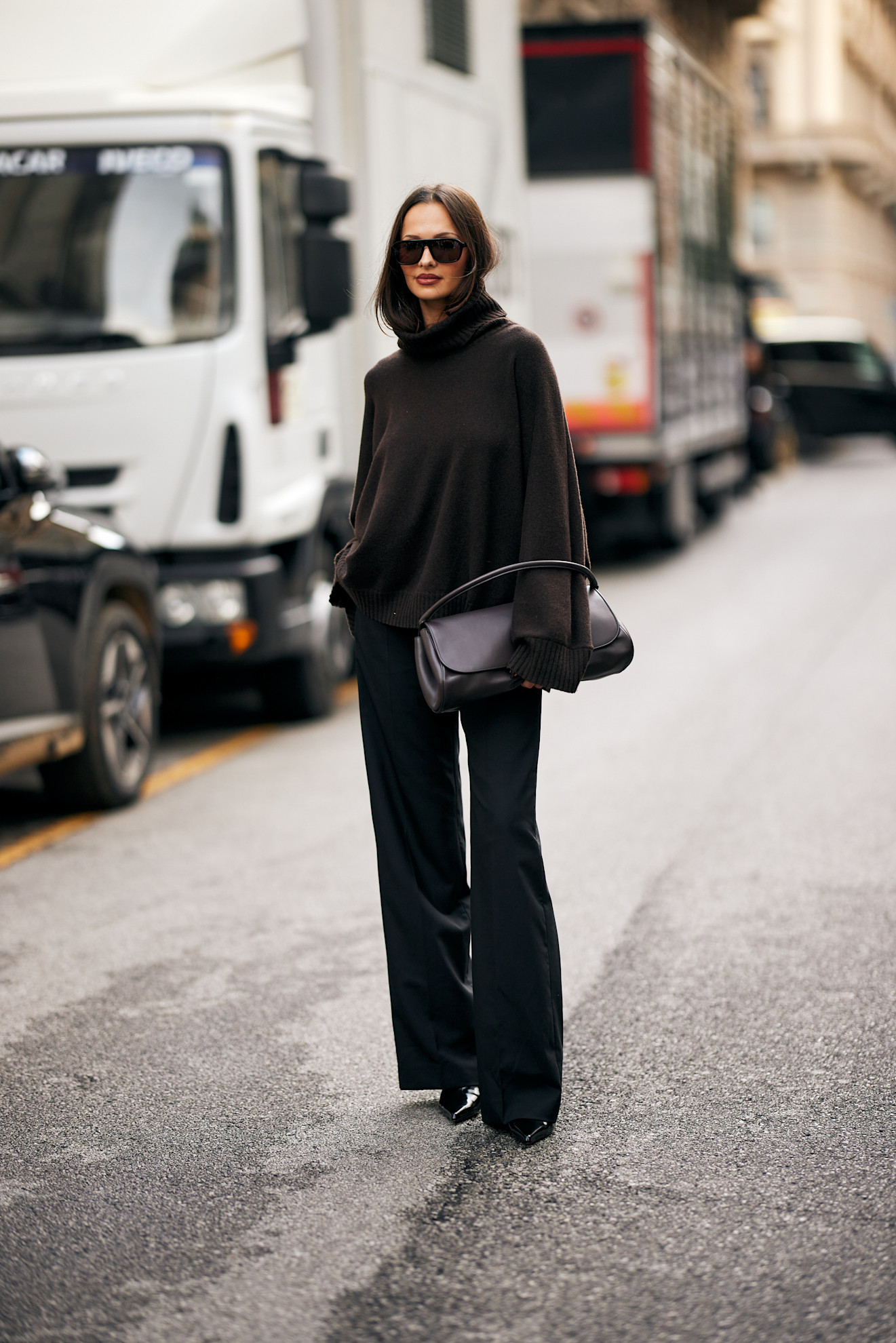 A woman in a brown oversized turtleneck and black trousers.