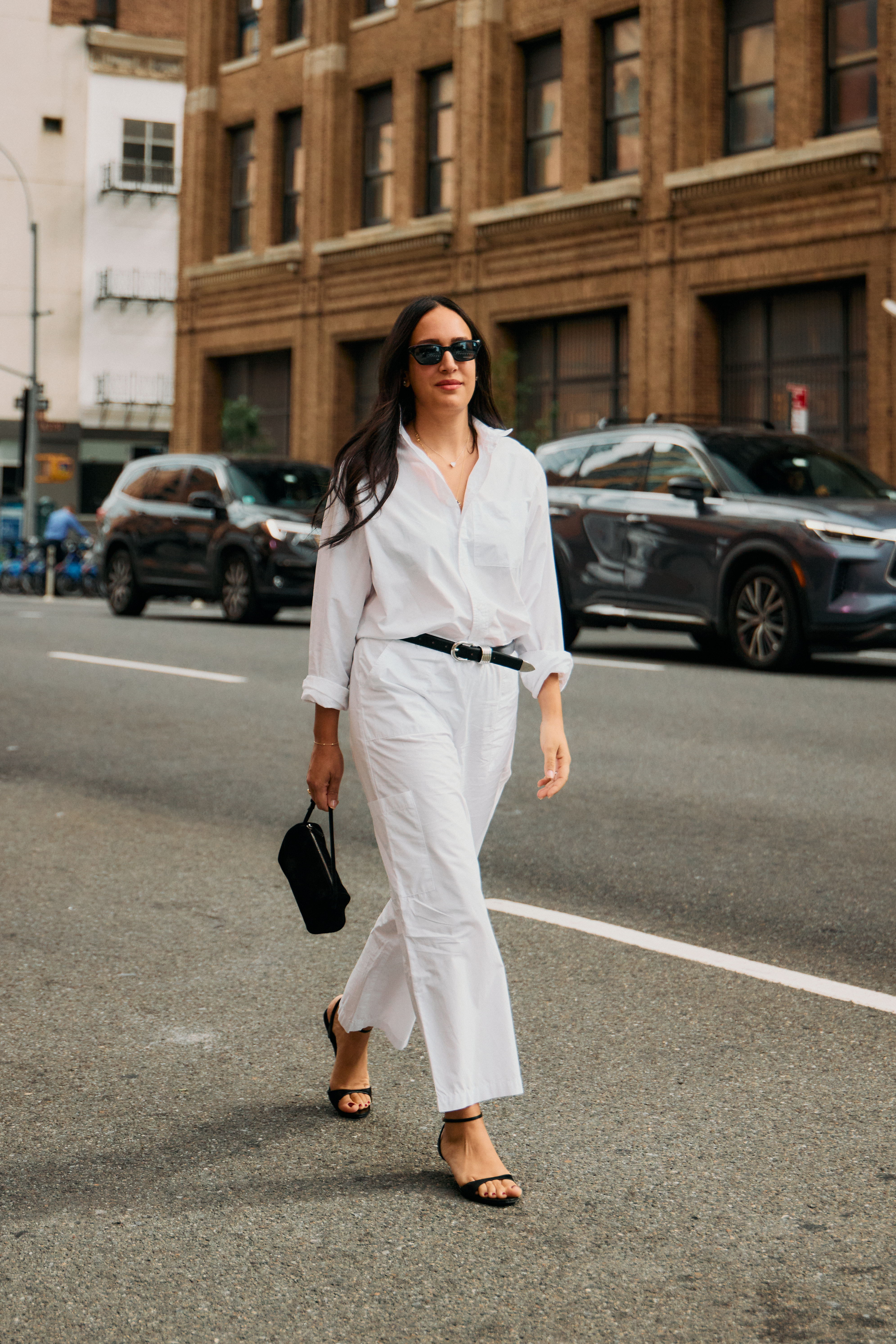 Woman in a white button-down, white pants, black open-toed heels, and a small black handbag.