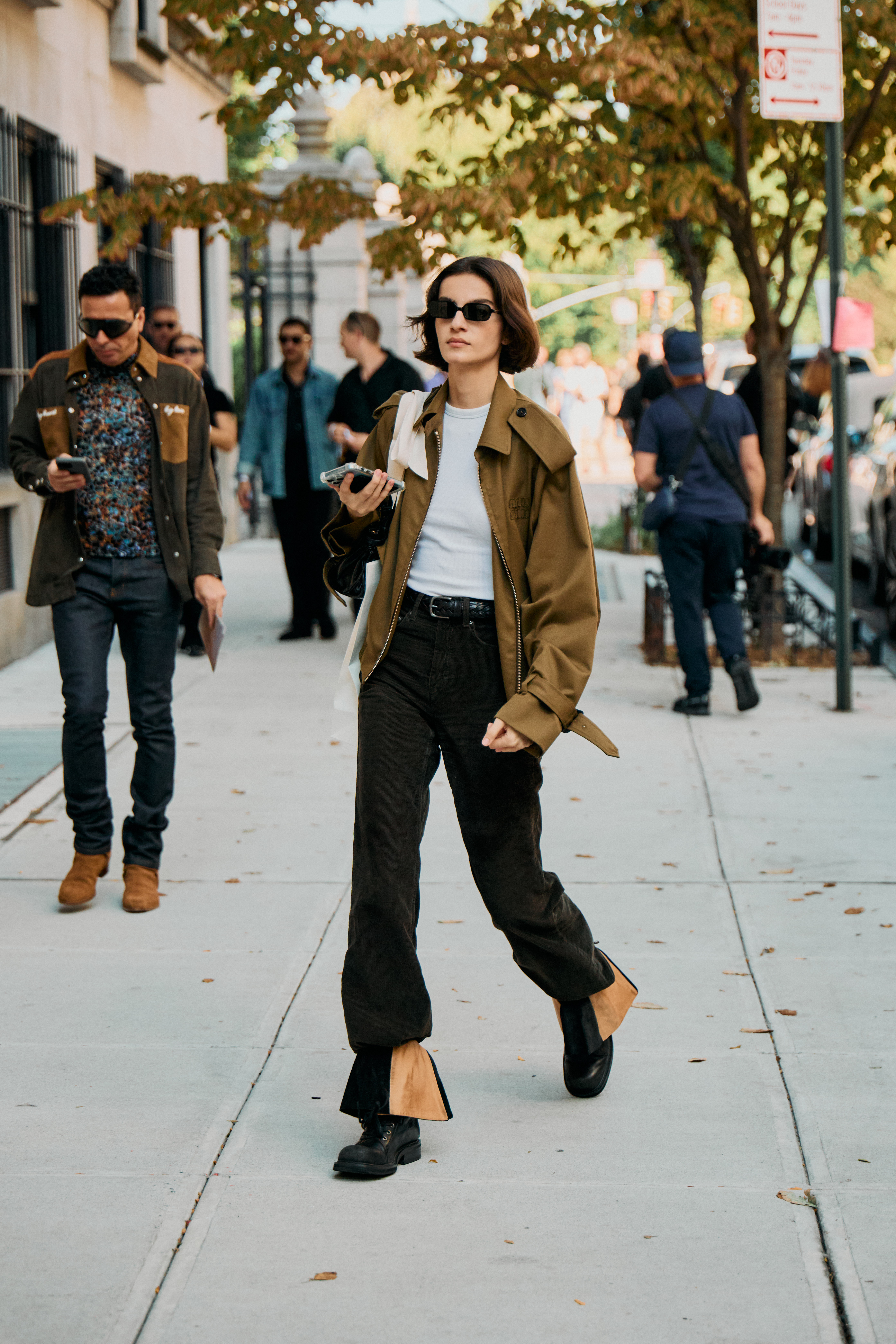 A person in a white crewneck, black jeans, and a cropped trench coat.