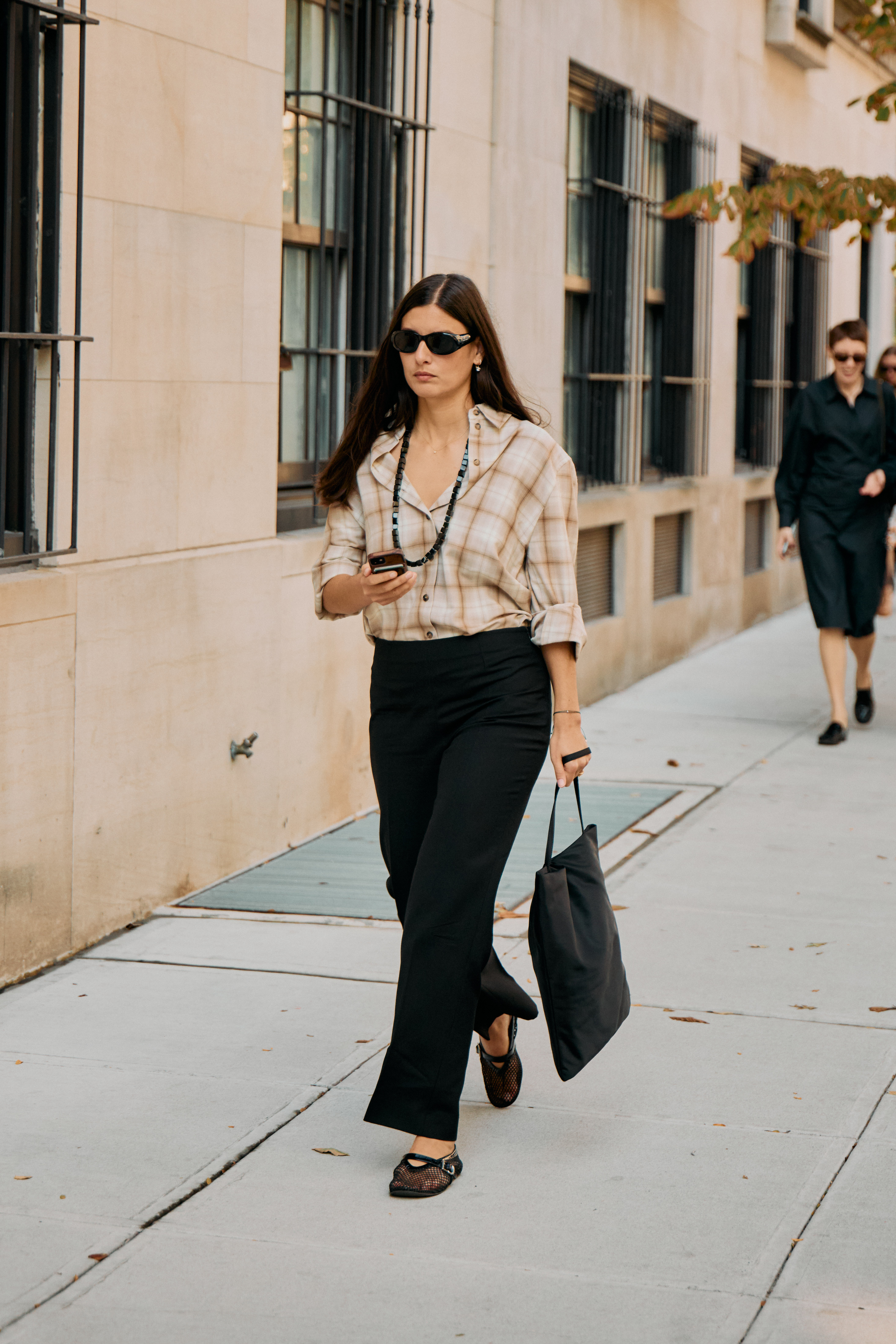 A woman in plaid button-down and black trousers with mesh flats and beaded necklace.