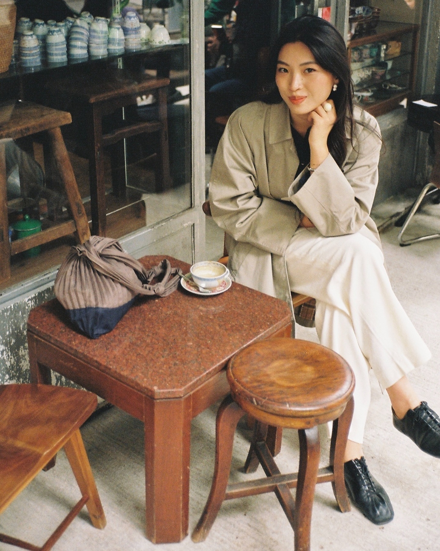 Influencer @michellelin.lin sits on a bench outfits wearing Derby shoes with cream trousers and a trend coat.