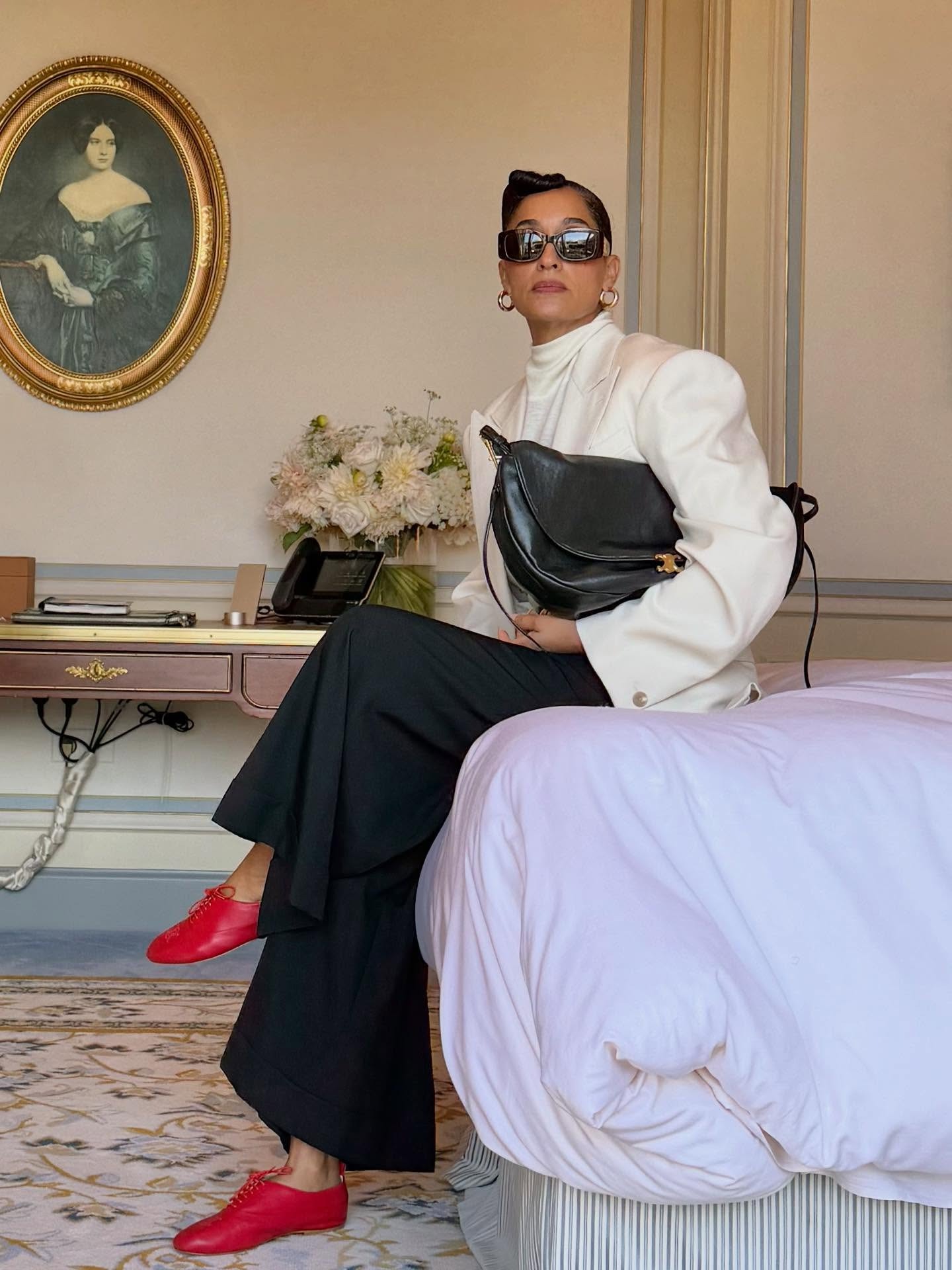 Tracee Ellis Ross wears red derby shoes with black trousers and a white high-neck blouse.