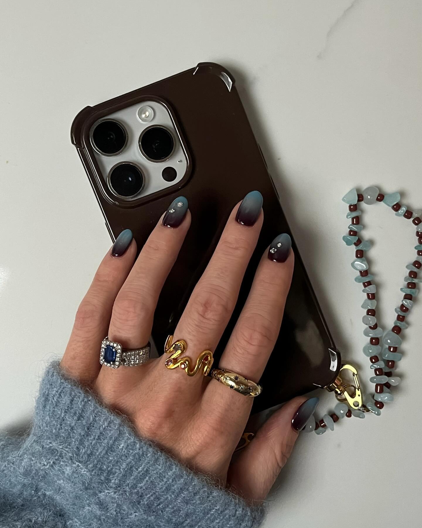 A woman holding a brown phone case with a brown and blue ombr&amp;eacute; nail design
