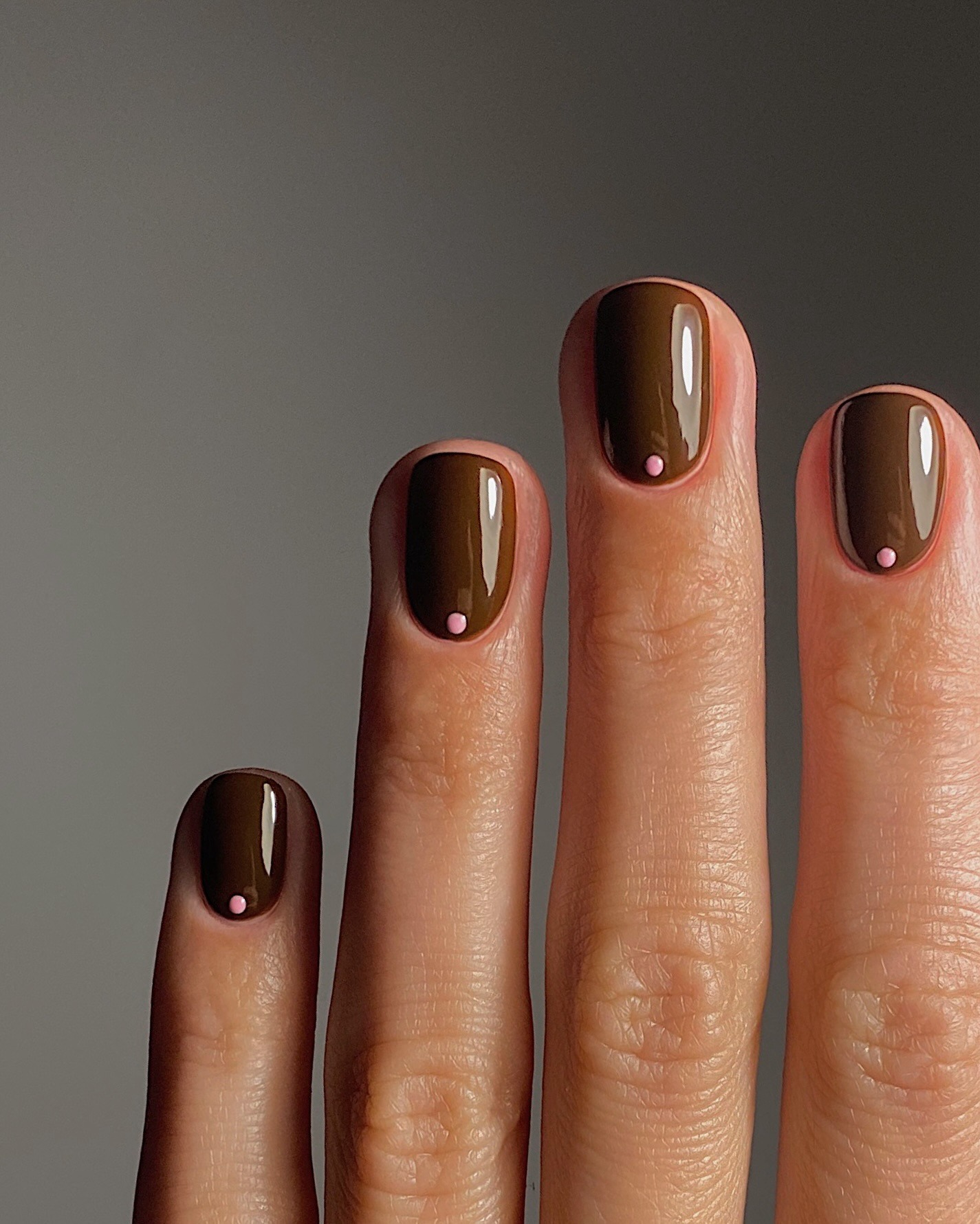 A brown manicure with micro pink polka dots at the base of the nail