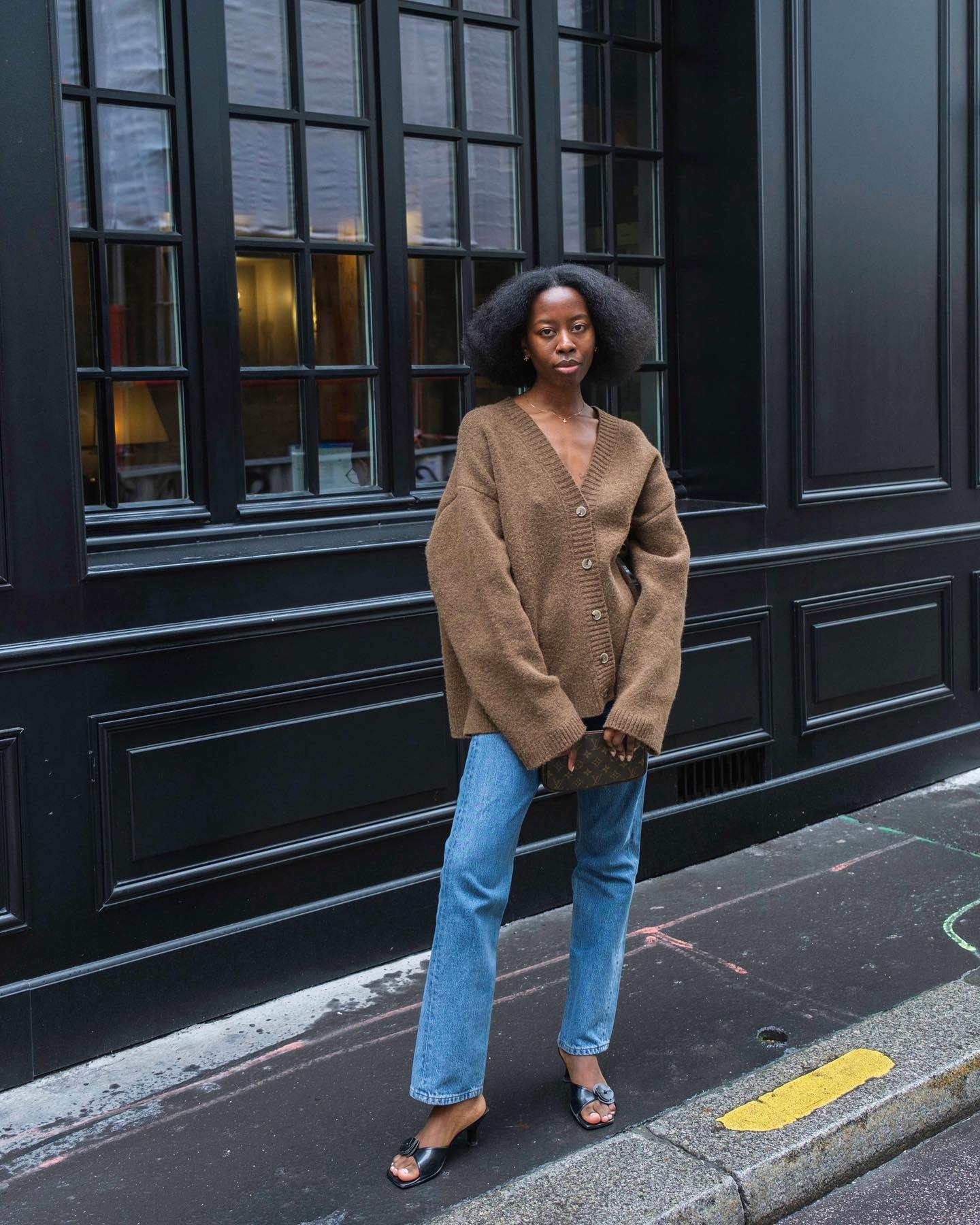Influencer @sylviemus_ wears a brown cardigan with blue jeans and black mules.