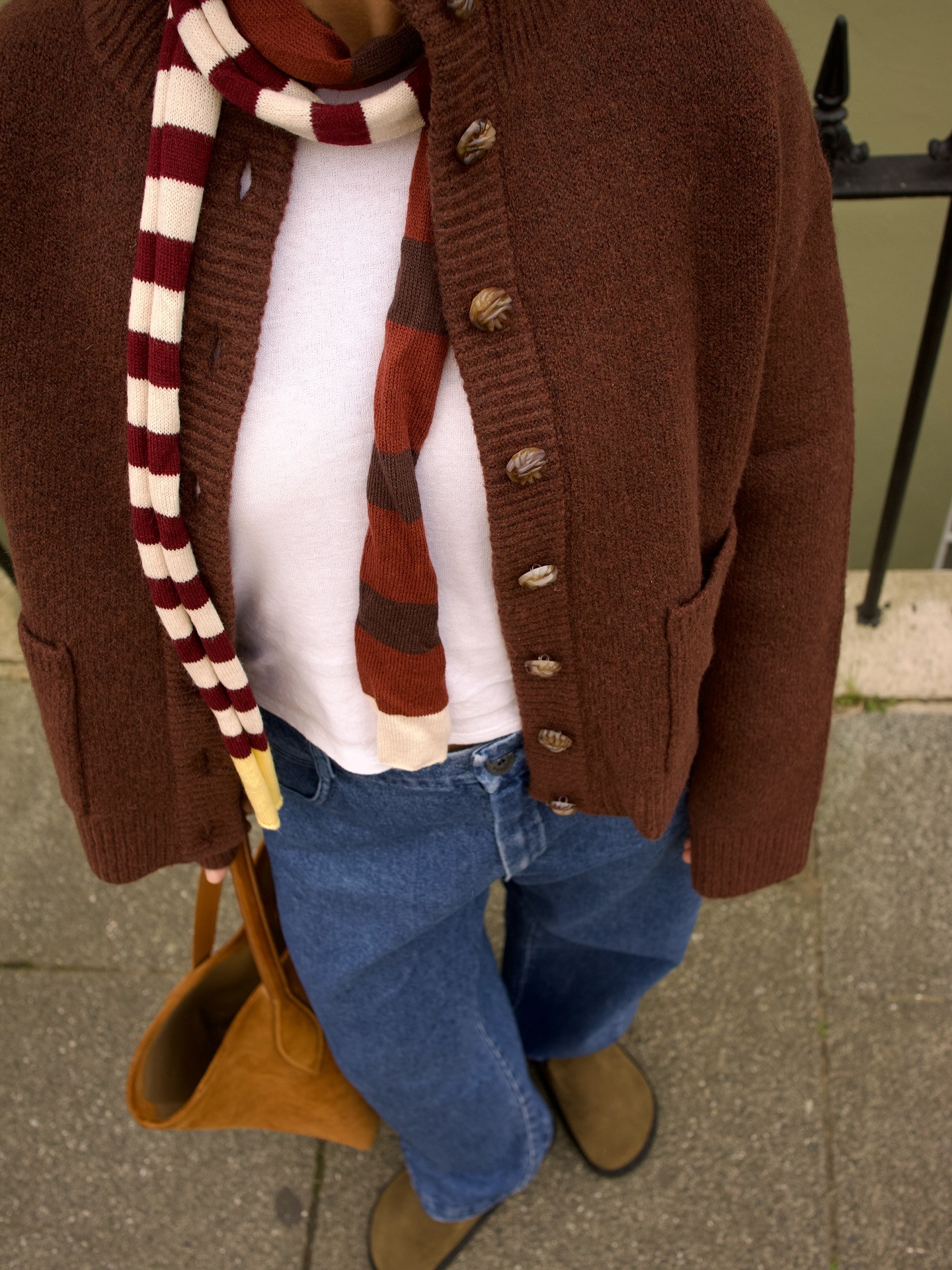 Influencer wears a brown cardigan with blue jeans and suede shoes.
