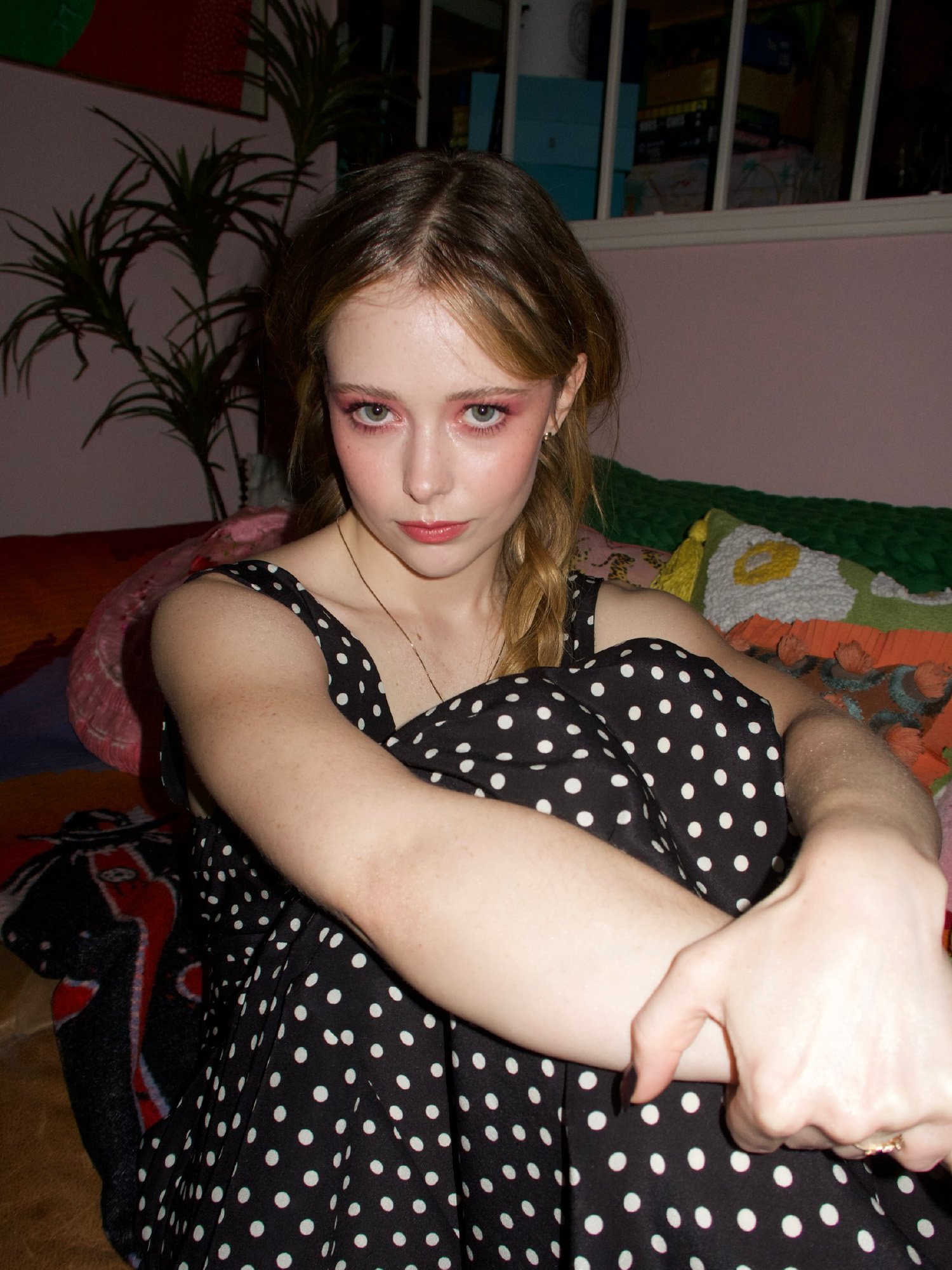 Actress Suzanna Son sitting in a chair with her arms clutched around her knees. She is wearing a polka dot dress.