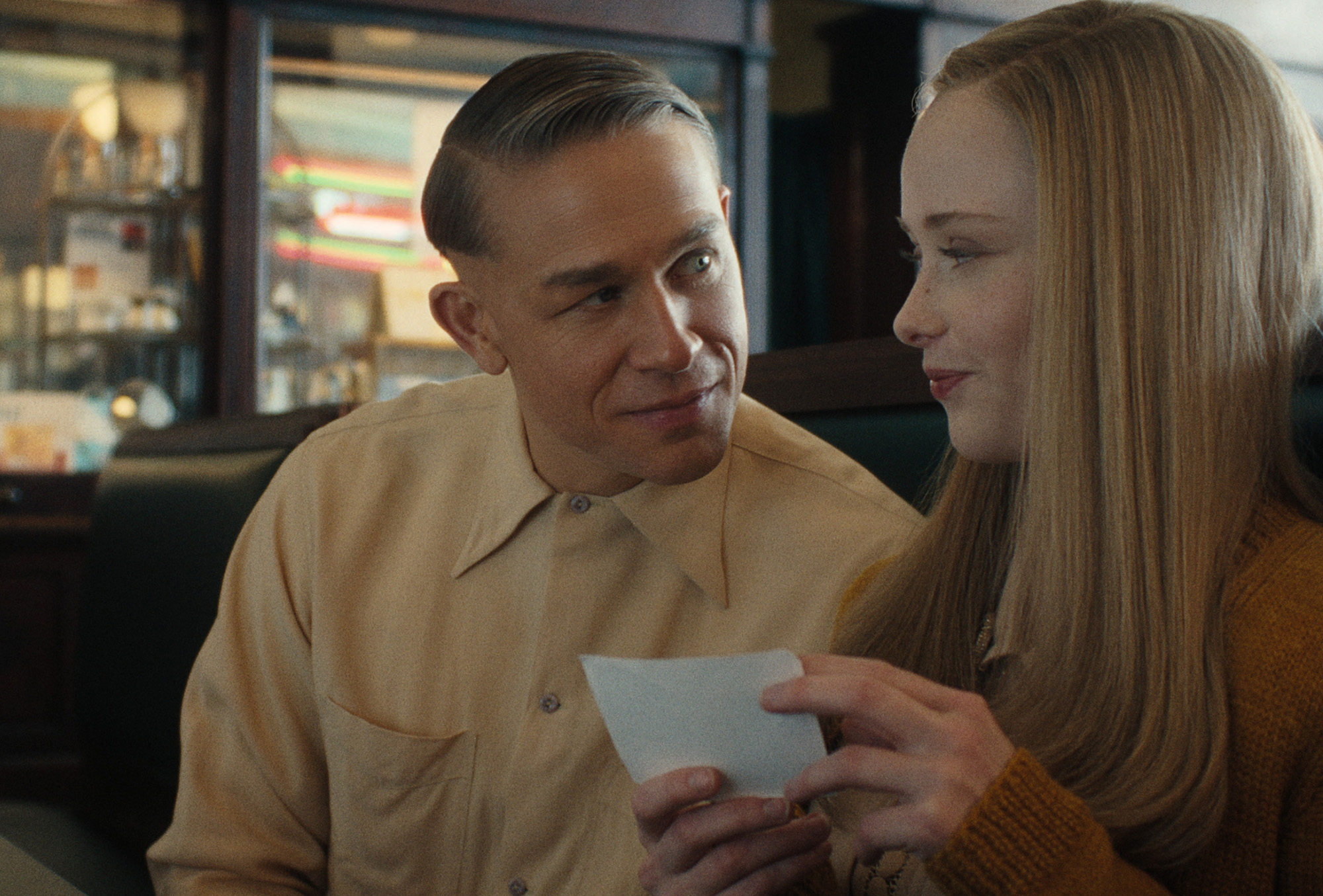 Still from Netflix&#039;s Monster: The Ed Gein Story. In the image you see characters Ed Gein, played by Charlie Hunnam, and Adeline Watkins, played by Suzanna Son, sitting together in a booth.