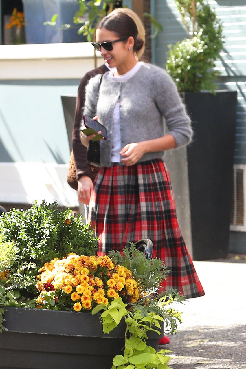 Olivia Rodrigo wearing a gray cardigan, white T-shirt, plaid skirt, socks, woven leather bag, and Mary Janes