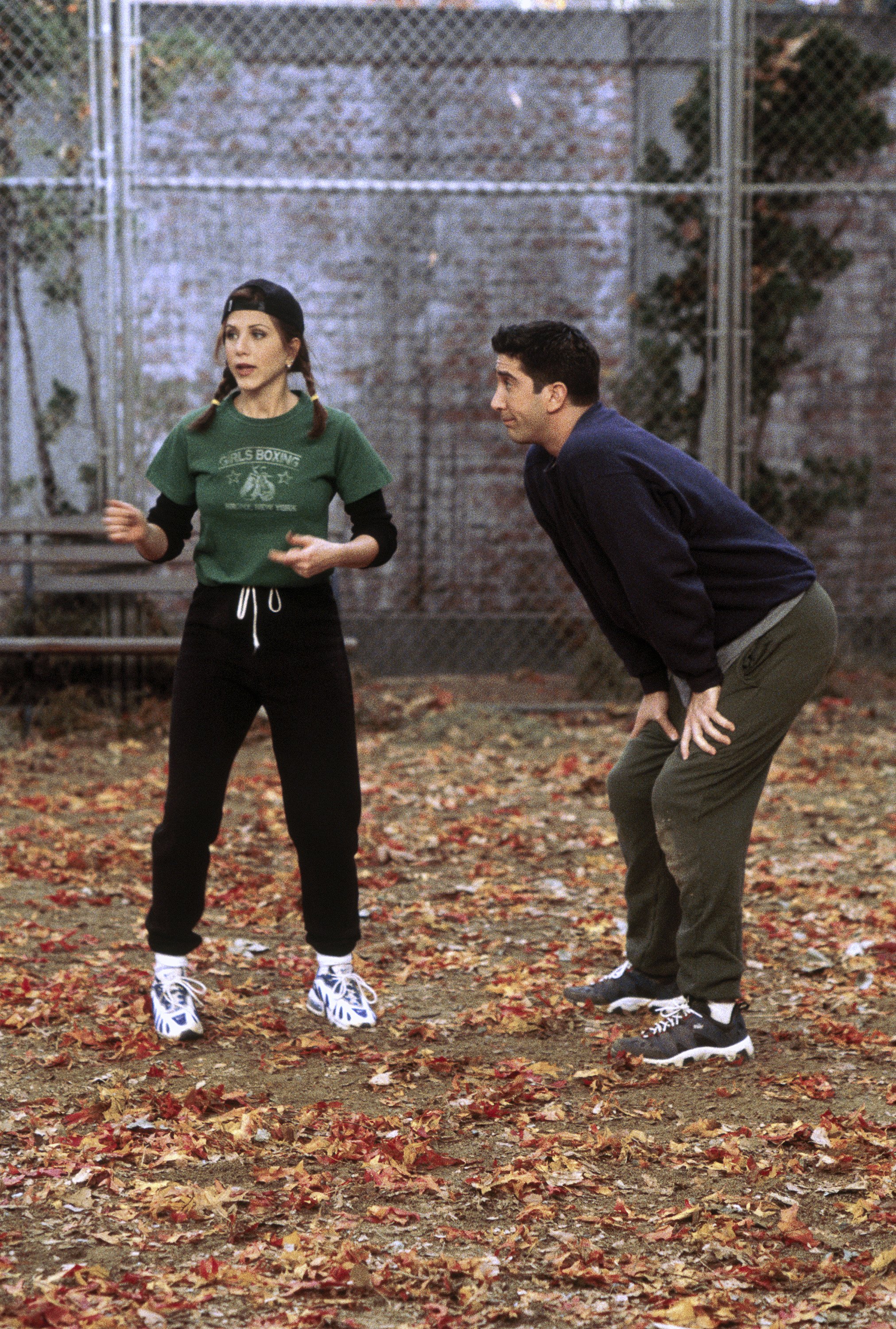 Jennifer Aniston as Rachel Green wears the layered t-shirt trend in friends in the 90&#039;s. She wears a green graphic cropped tee. A black long sleeve, black tracksuit bottoms and a nike trainer. This mage was taken from Getty.