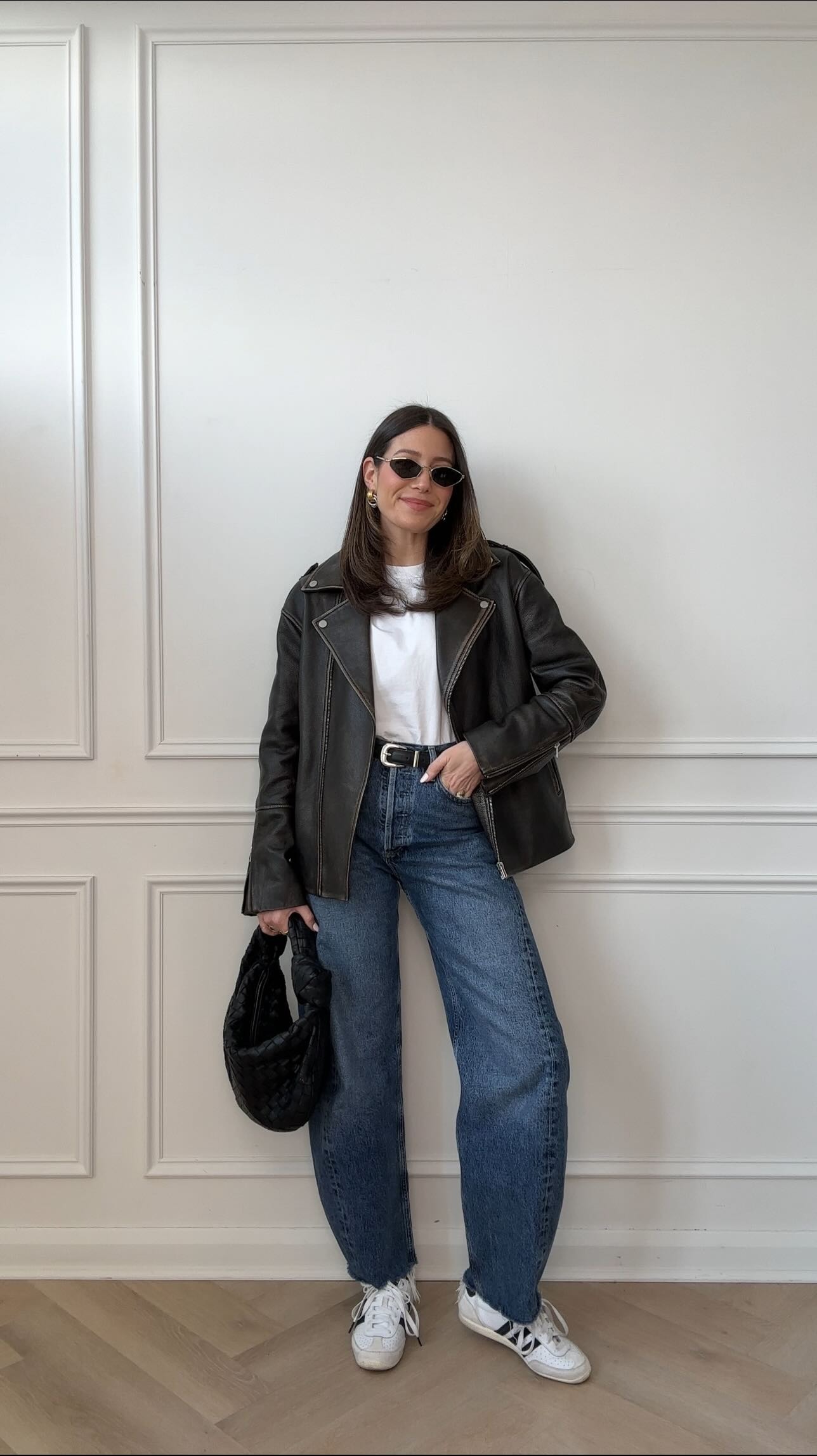 woman wears white tshirt, jeans, leather jcaket, and black handbag along with adidas japan shoes