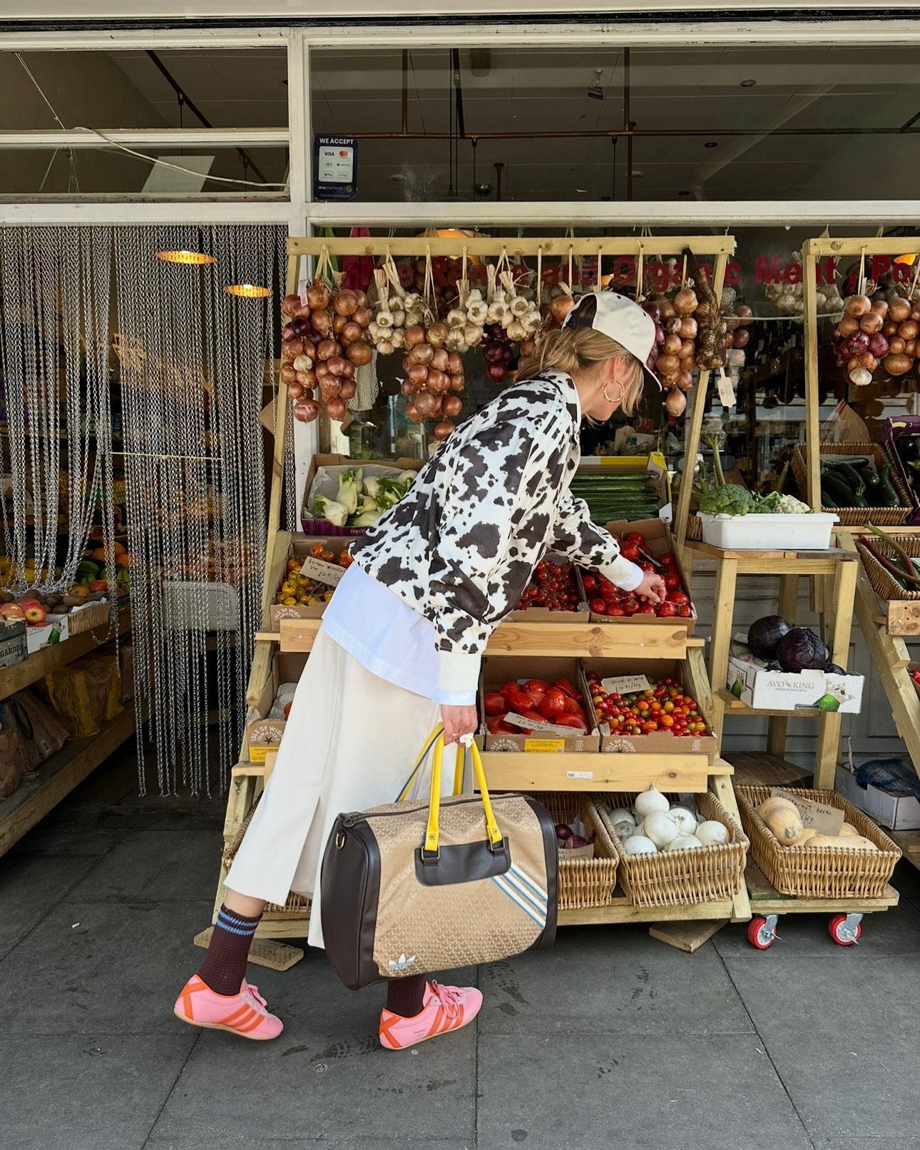 torivan wears cowprint jacket, skirt, and pink adidas tokyo shoes while picking produce