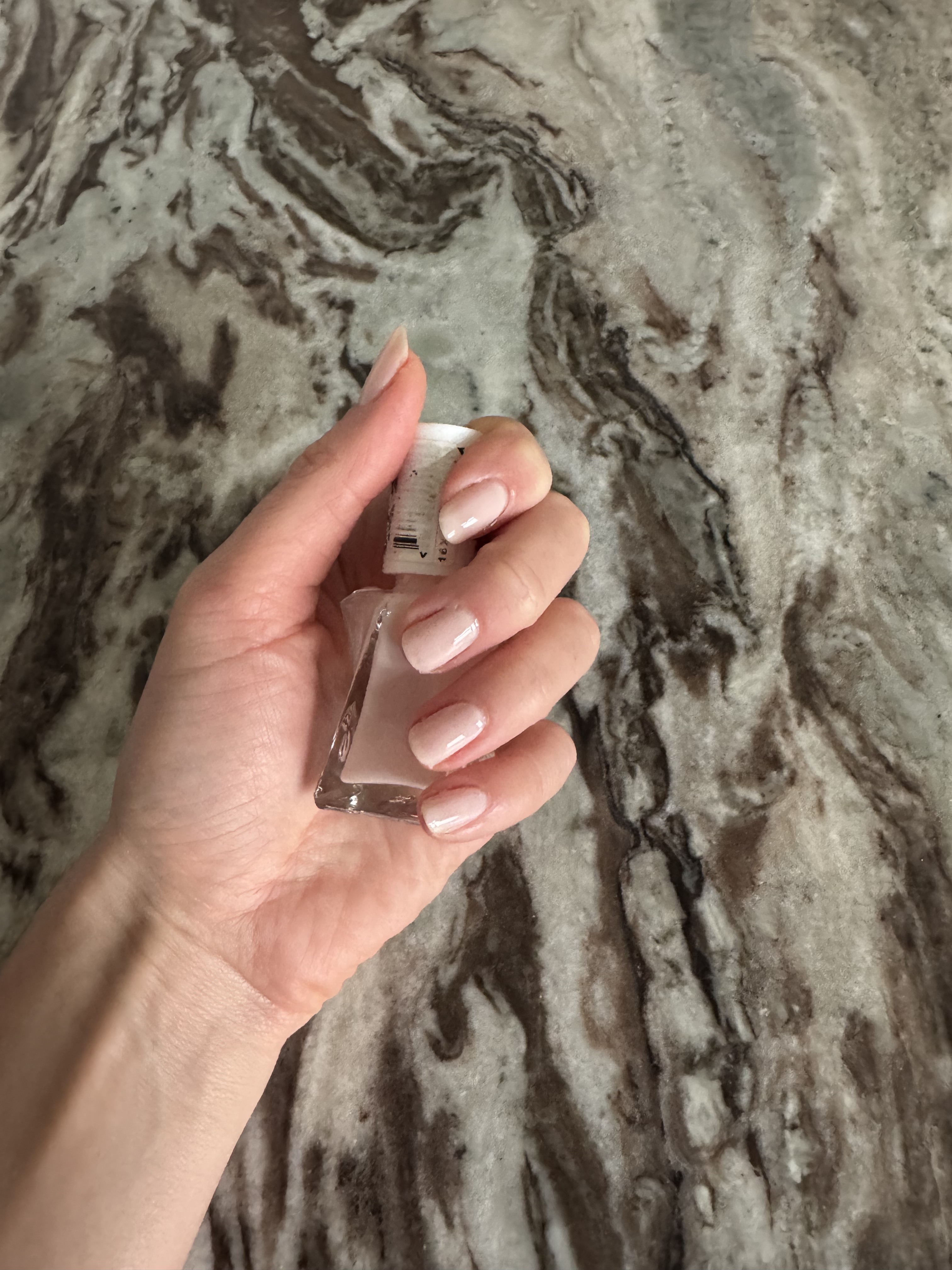 Eleanor holding a bottle of Essie Gel Couture in the shade Fairy Tailor, a sheer pink nail colour which she has also painted her nails with