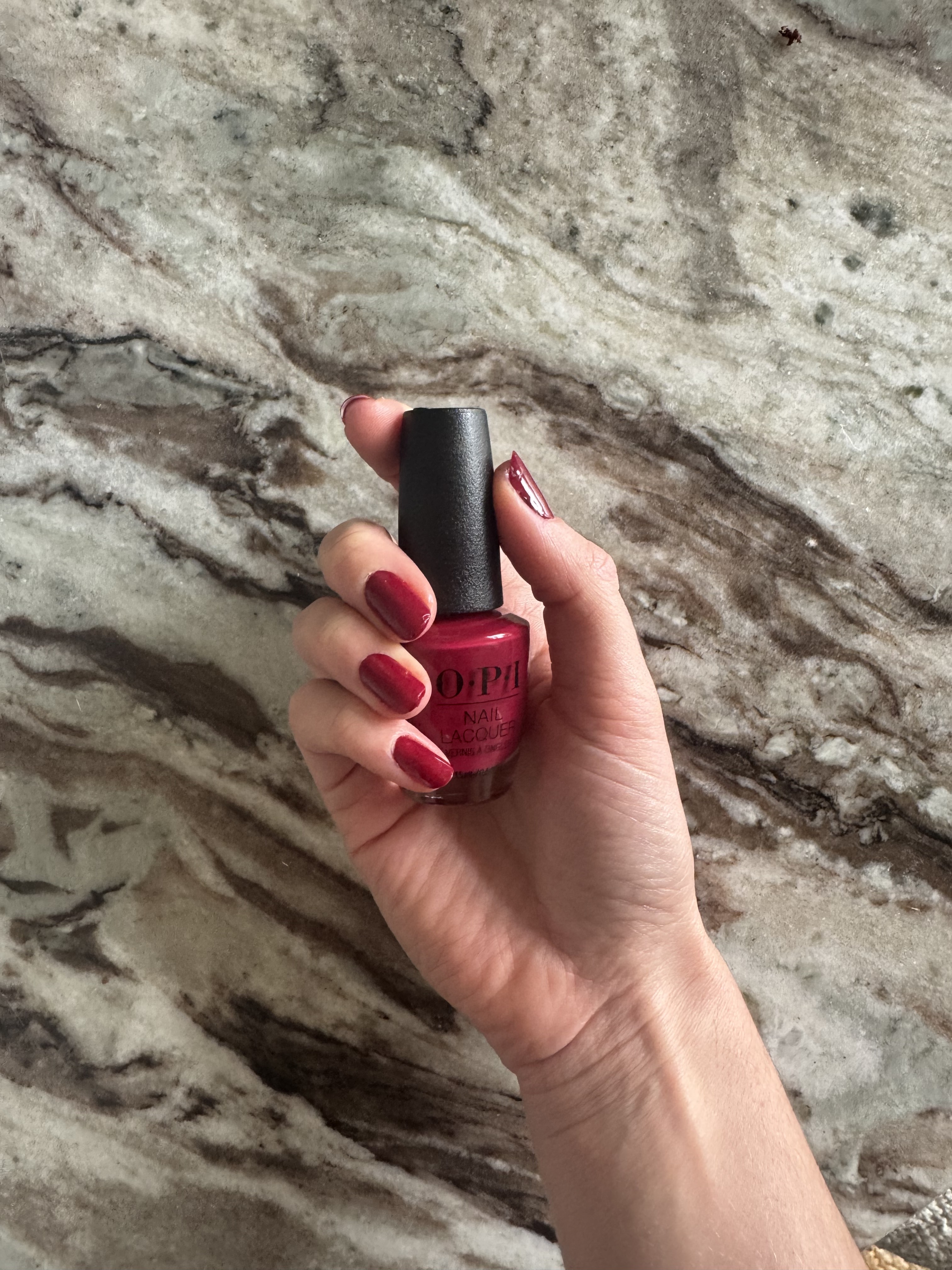 Eleanor holding a bottle of OPI nail lacquer in the shade Malaga Wine, which is also painted on her nails