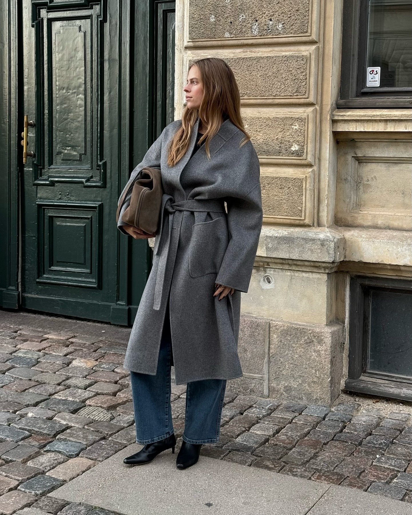 Influencer @claradyrhauge wears a grey wrap coat with blue jeans and black kitten heel boots.