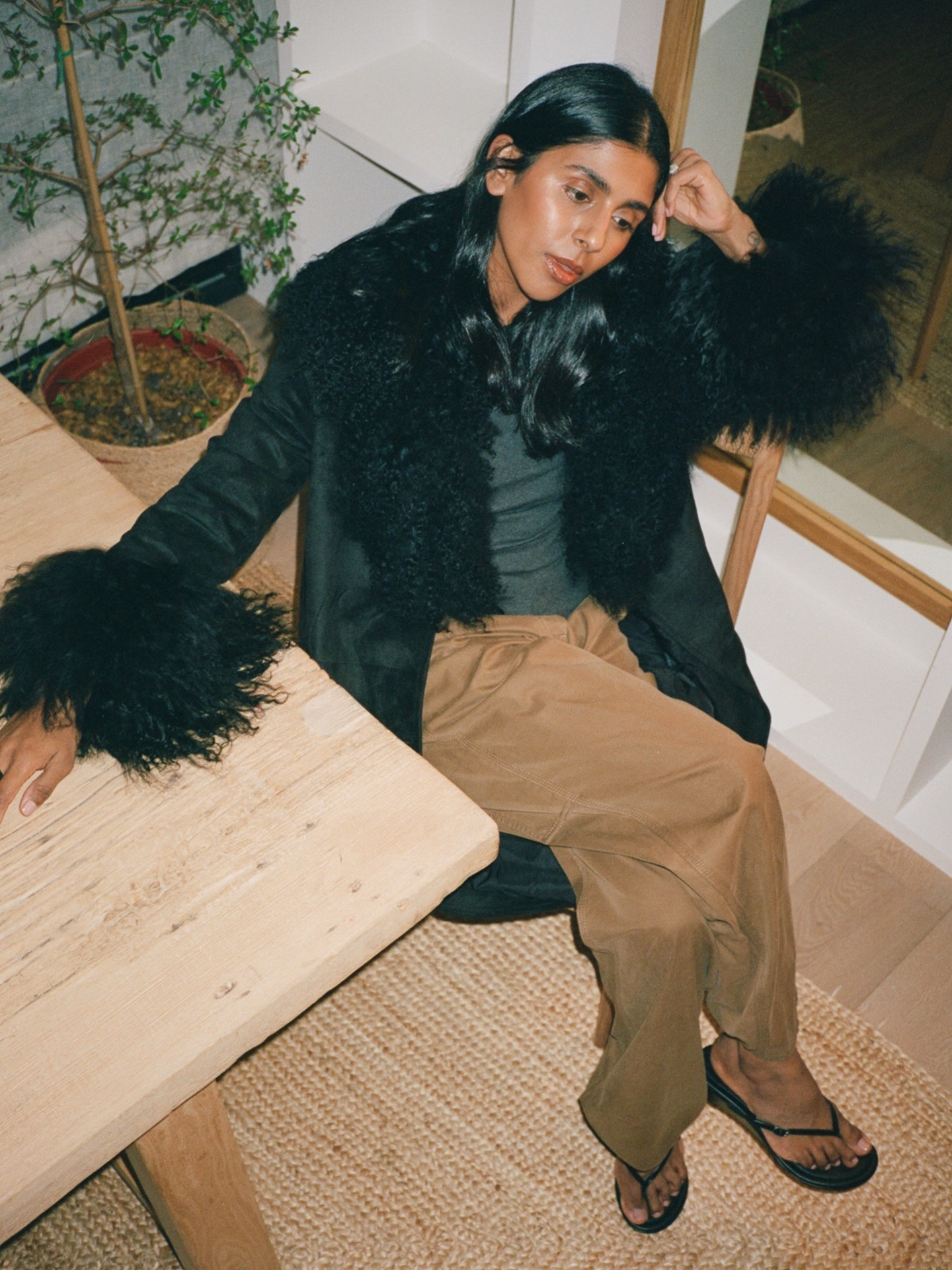 Monikh wears a black Penny Lane coat, beige trousers, and flip-flops.