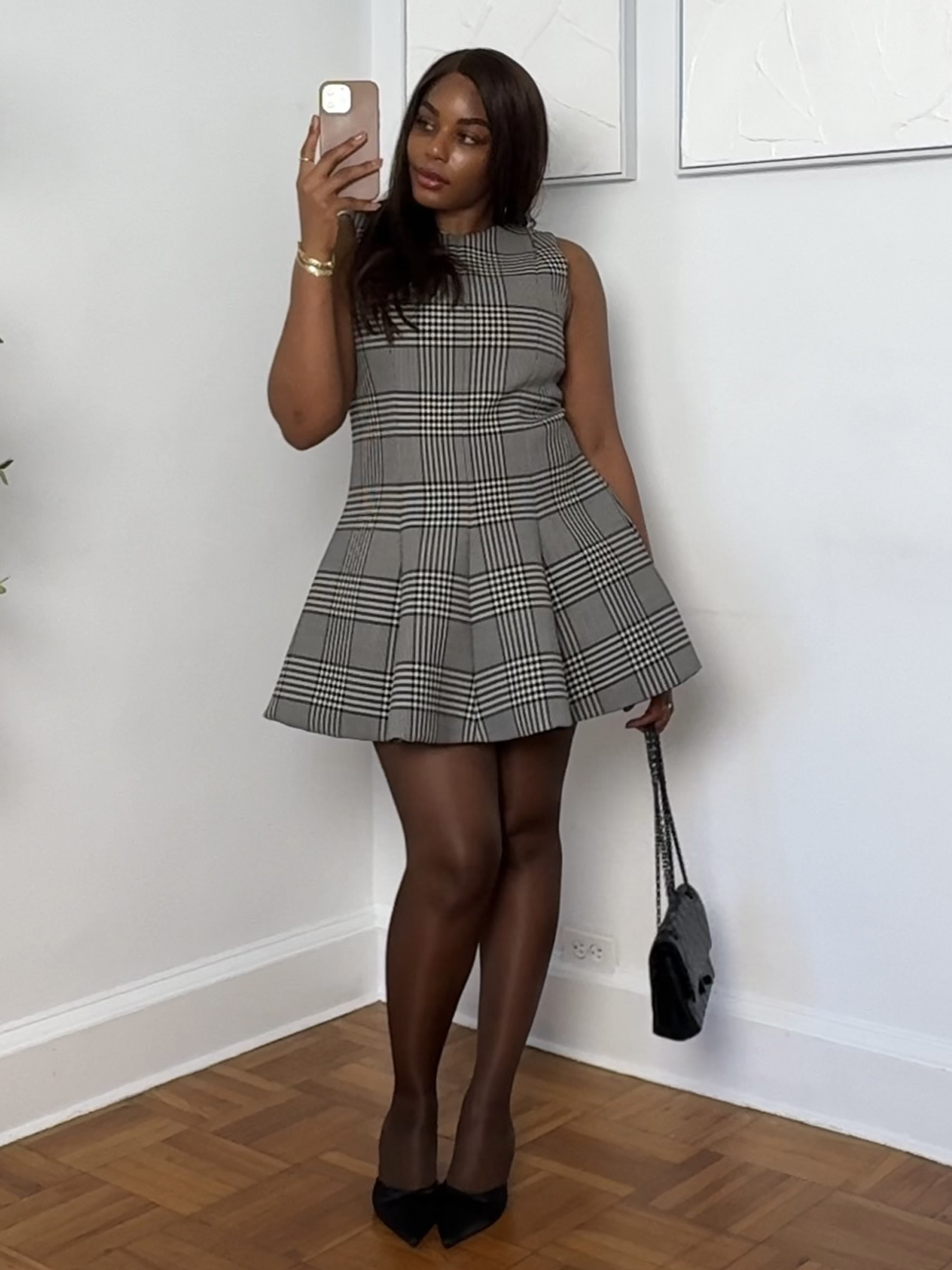 fashion and beauty influencer Kaye Bassey poses in her NYC apartment wearing a winter 2025 2026 outfit with houndstooth plaid Brandon Maxwell dress, black sheer tights, and pumps