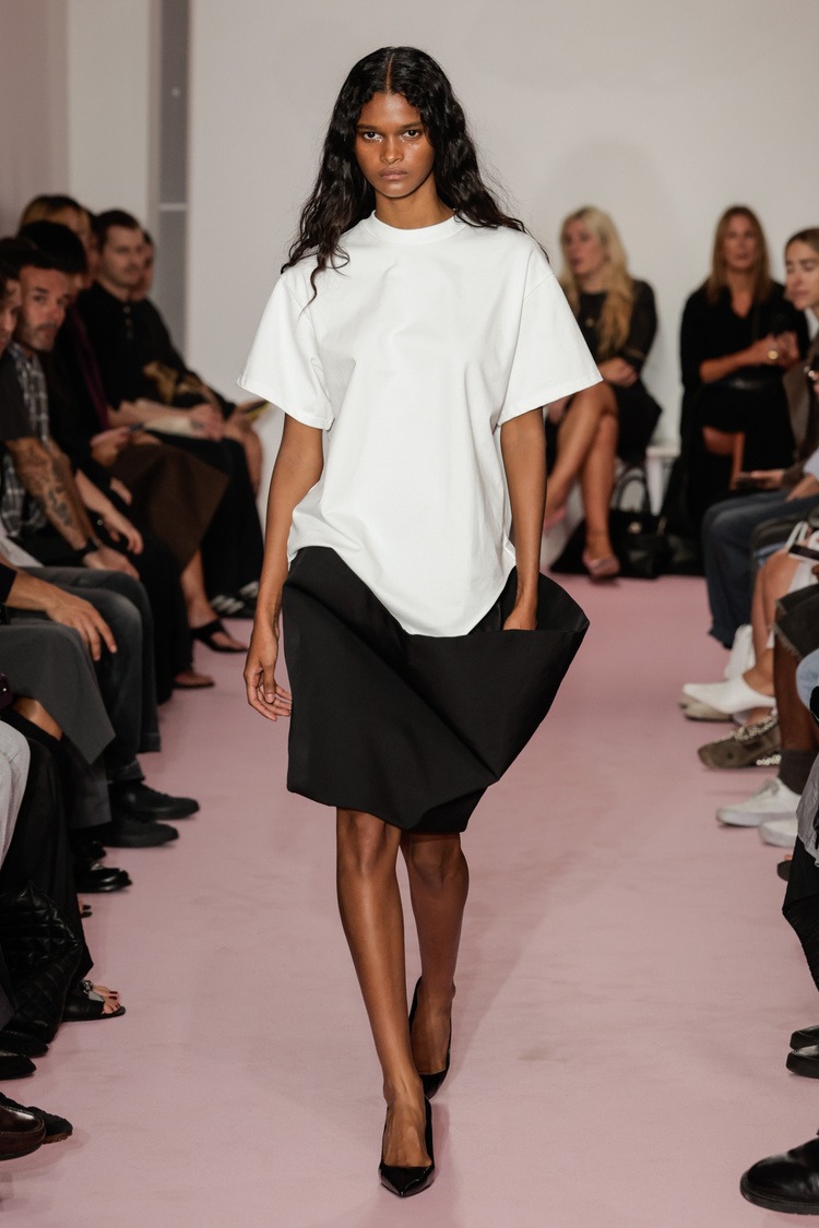 A model at the Lii Spring Summer 2026 runway show wearing a white T-shirt and a black skirt.