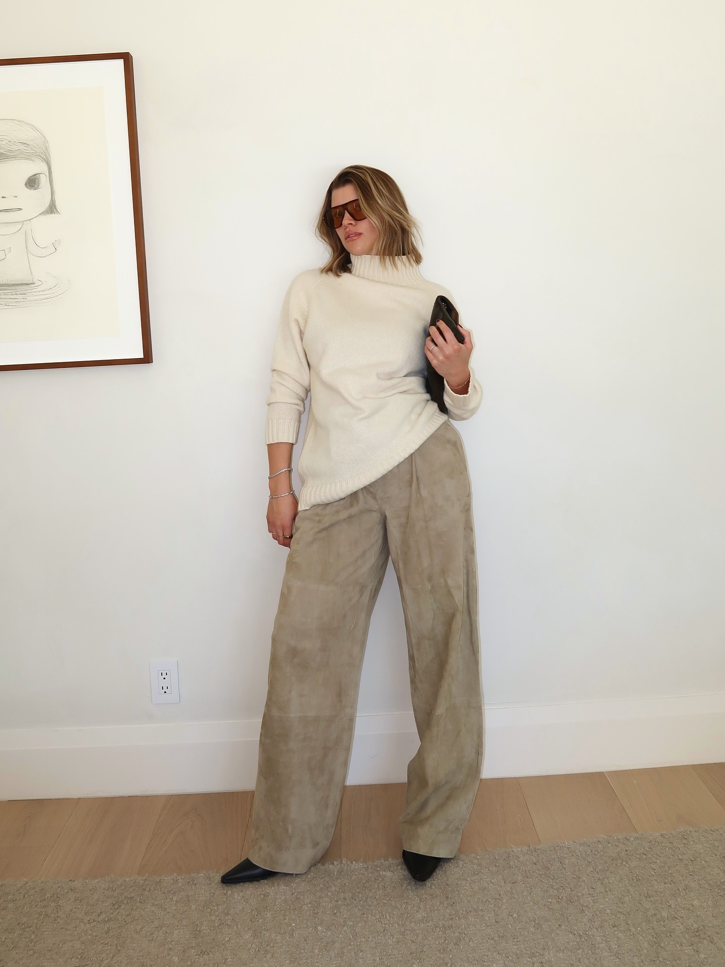 Sofia wears a white turtleneck, beige suede pants, and black pointed toe boots.